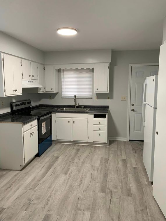 A kitchen with white cabinets , a stove , a sink , and a refrigerator.