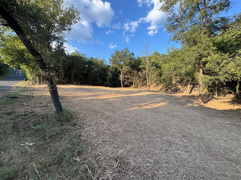 Cleared land covered in wood chips, surrounded by trees and blue sky.