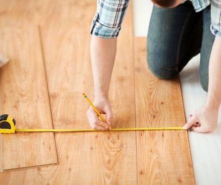 A man is measuring a wooden floor with a tape measure.