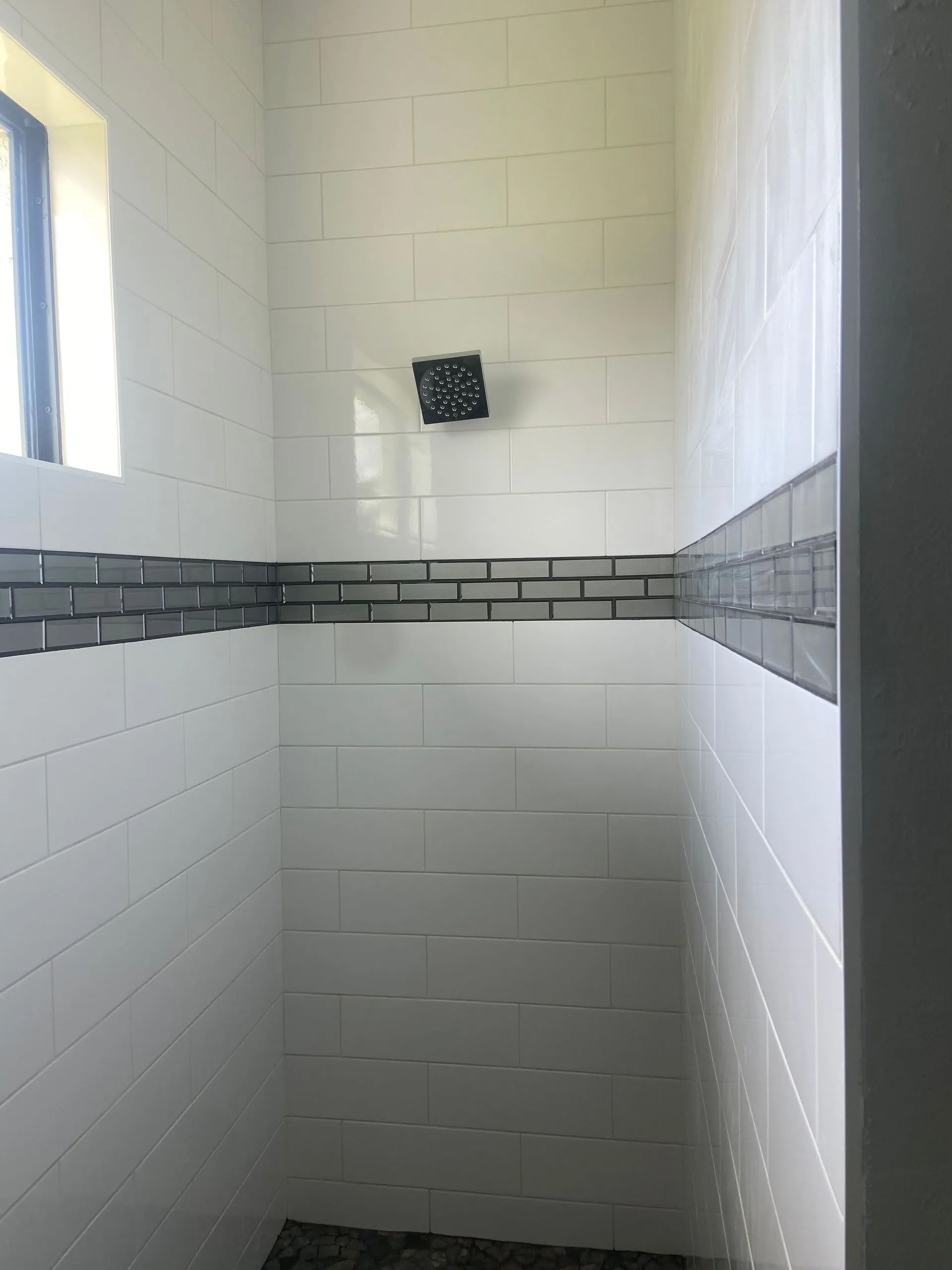 A shower with white tiles and a black shower head.