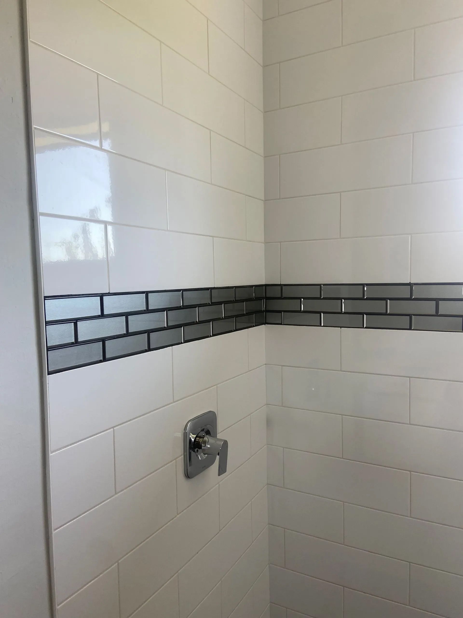 A shower with white tiles and a gray brick border.