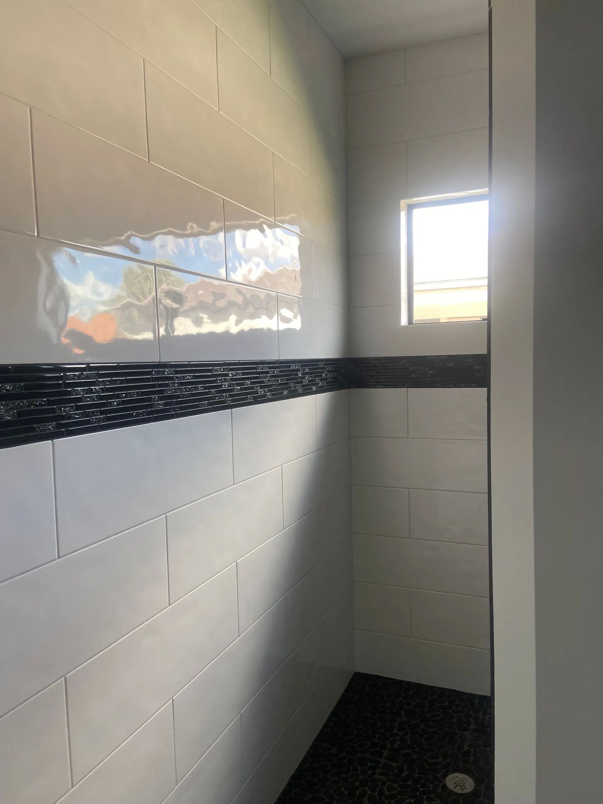A bathroom with white tiles and a black floor and a window.