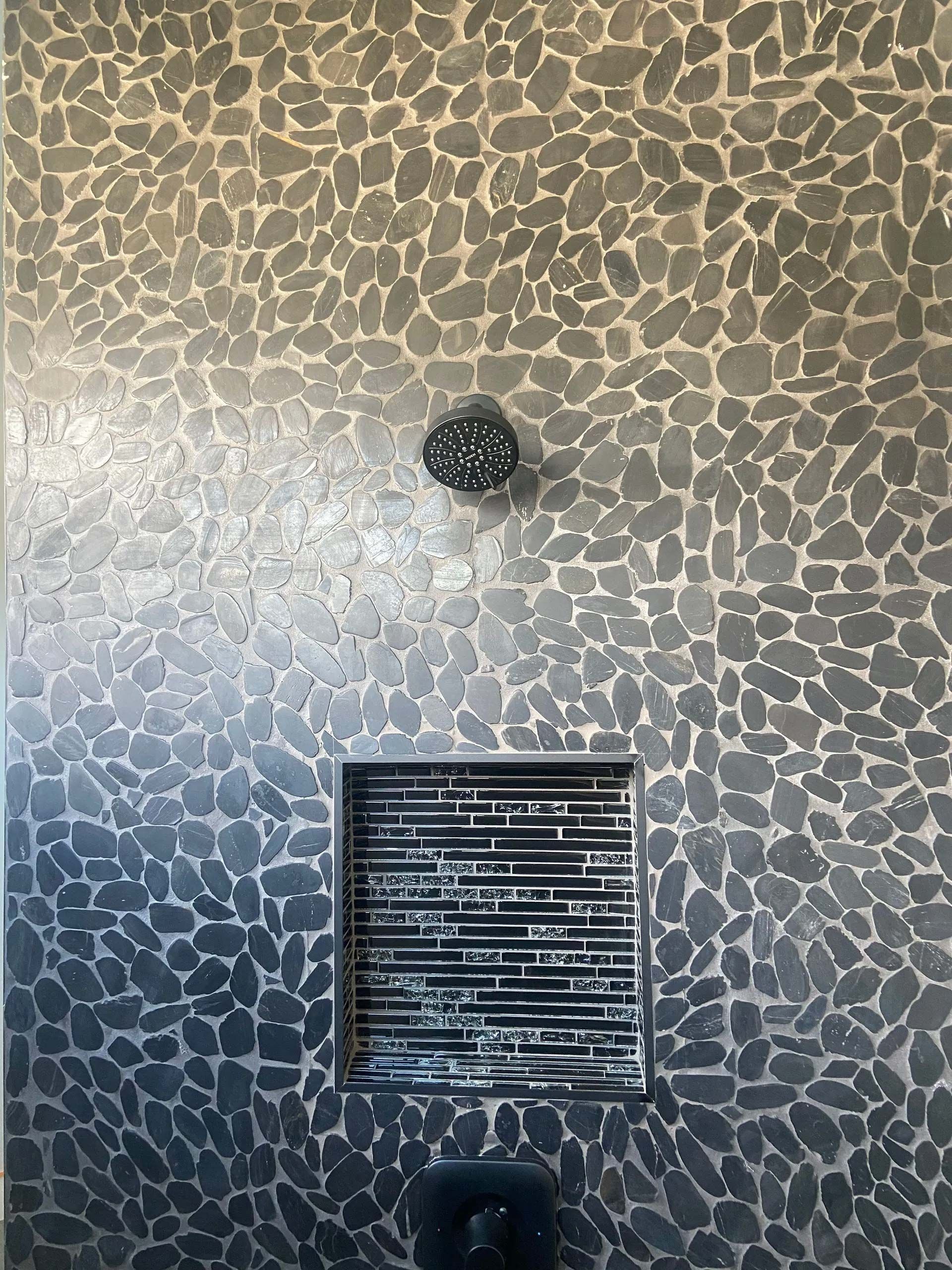 A shower head is mounted on a wall with a mosaic pattern.