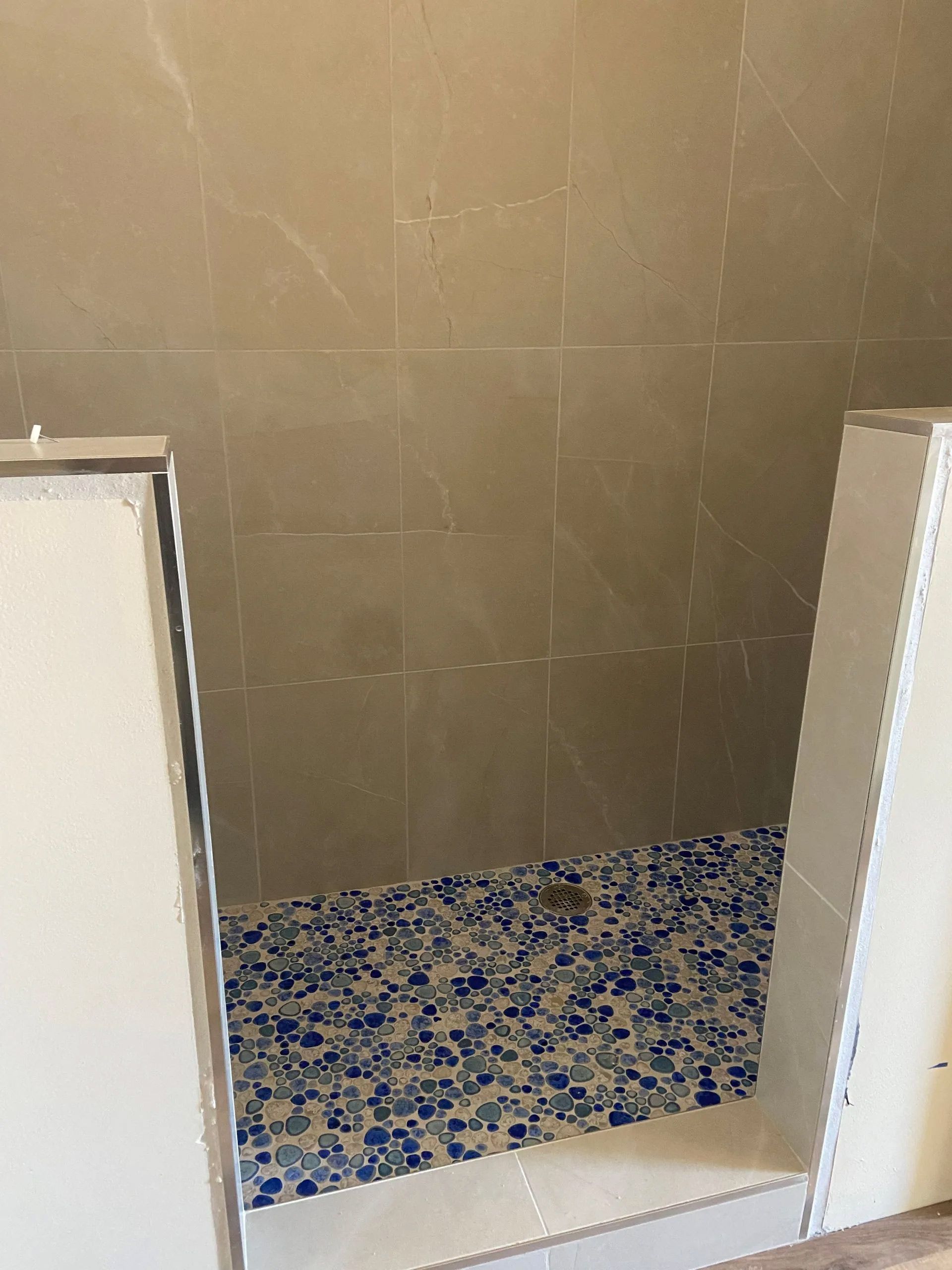 A bathroom with a walk in shower with blue and white tiles.