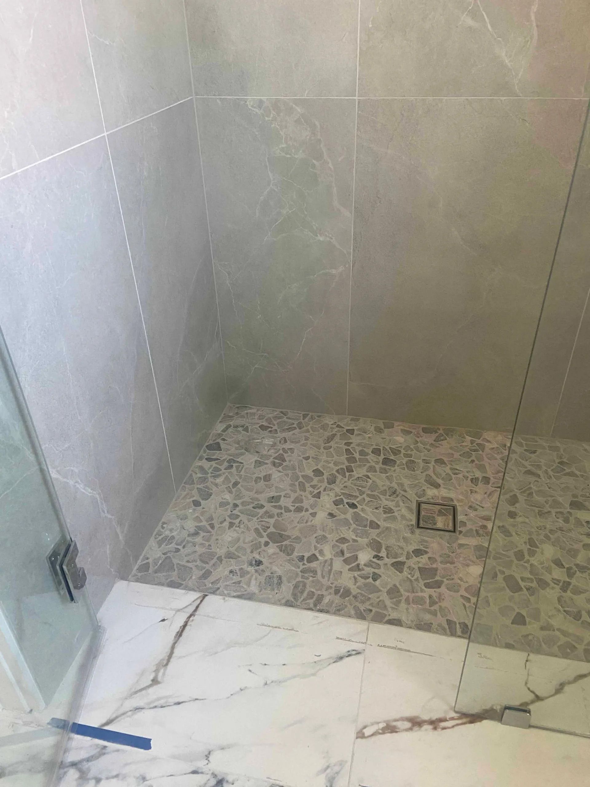 A walk in shower with a tiled floor and a glass door.