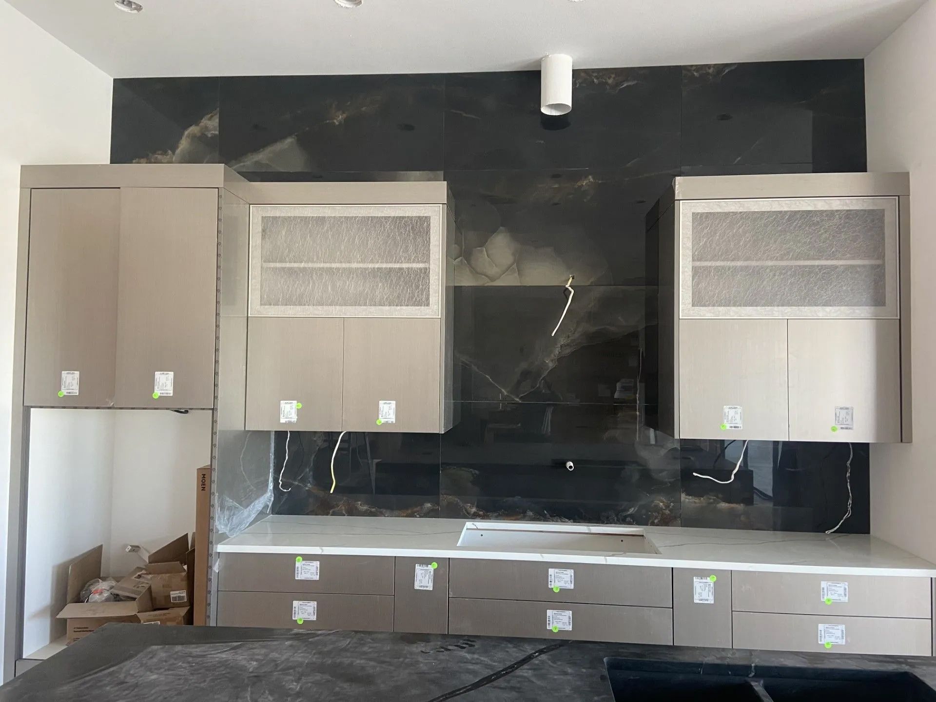 A kitchen with a black tile wall and white cabinets.