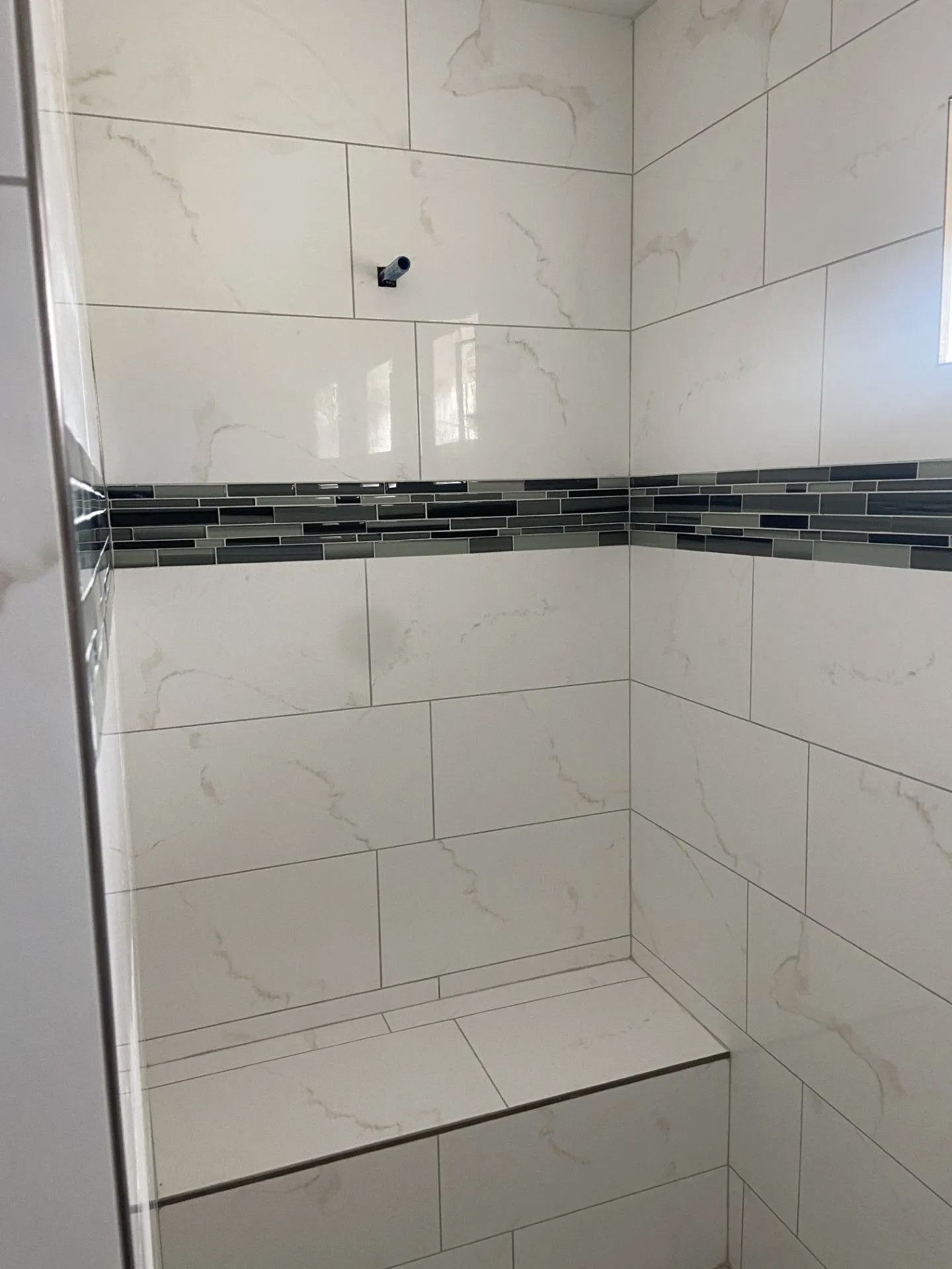A shower with white tiles and a bench in it.