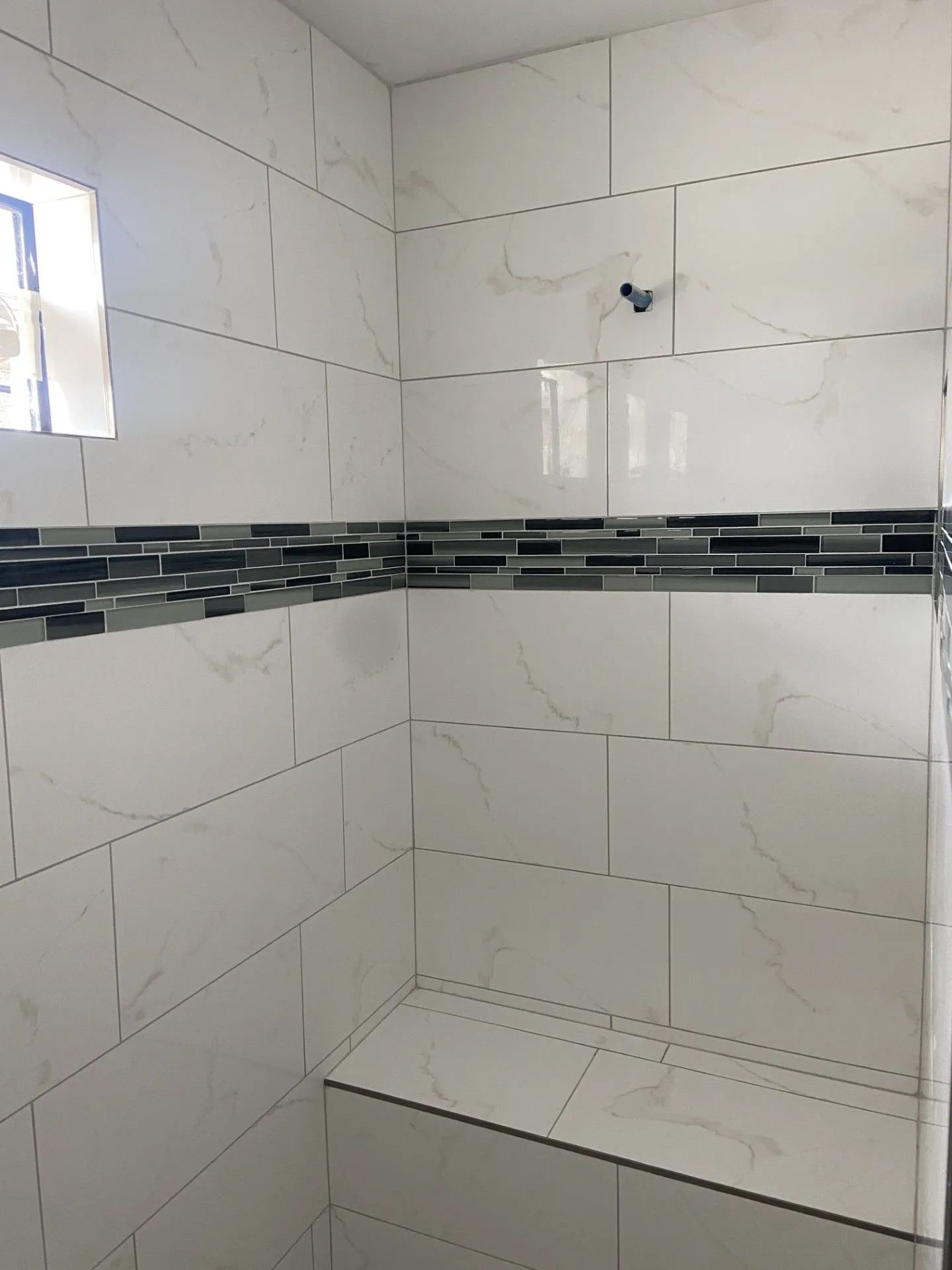 A bathroom with white tiles and a shower head.