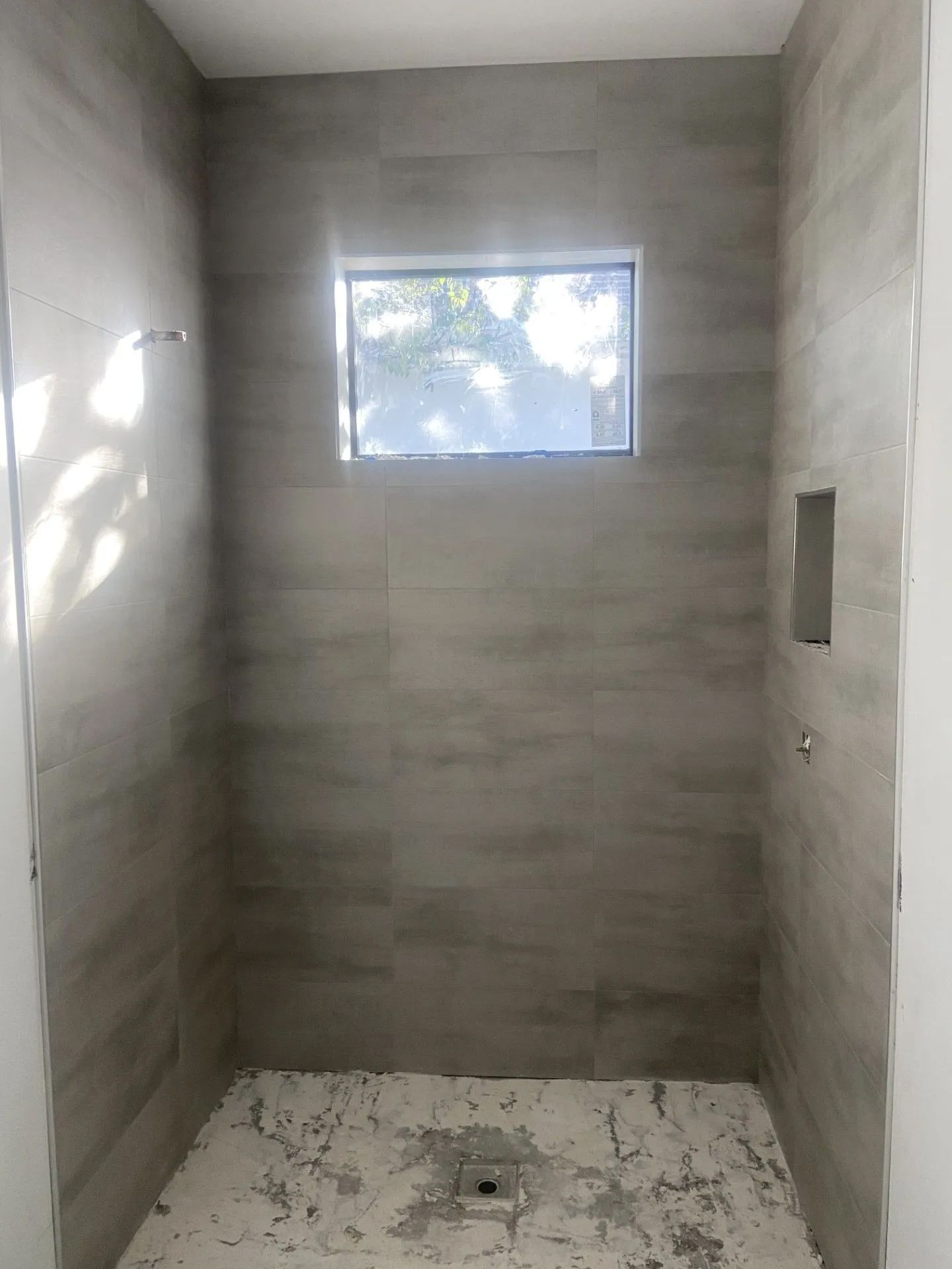 A shower stall with a window and a tiled floor.