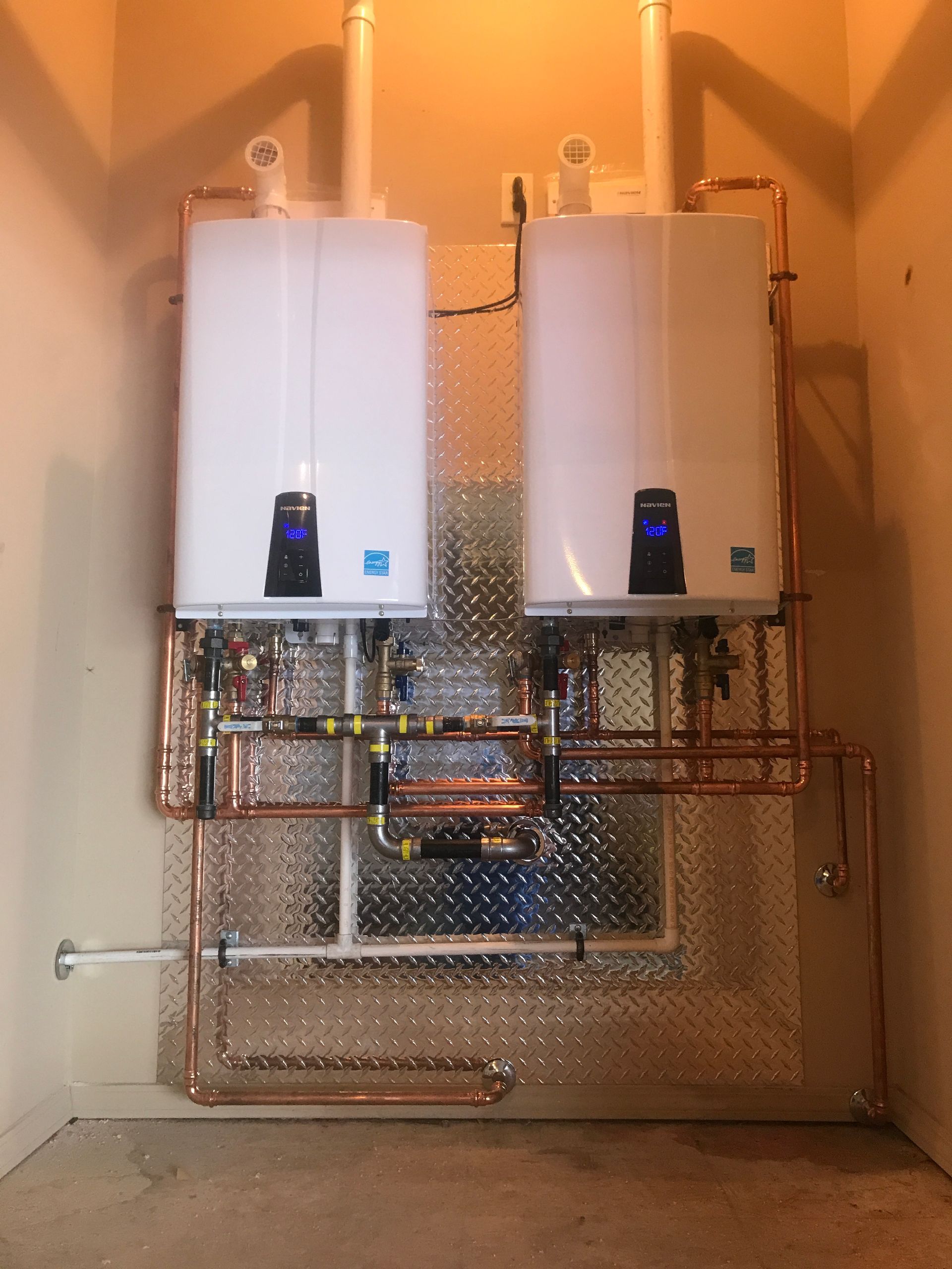 Two water heaters are connected to copper pipes in a room