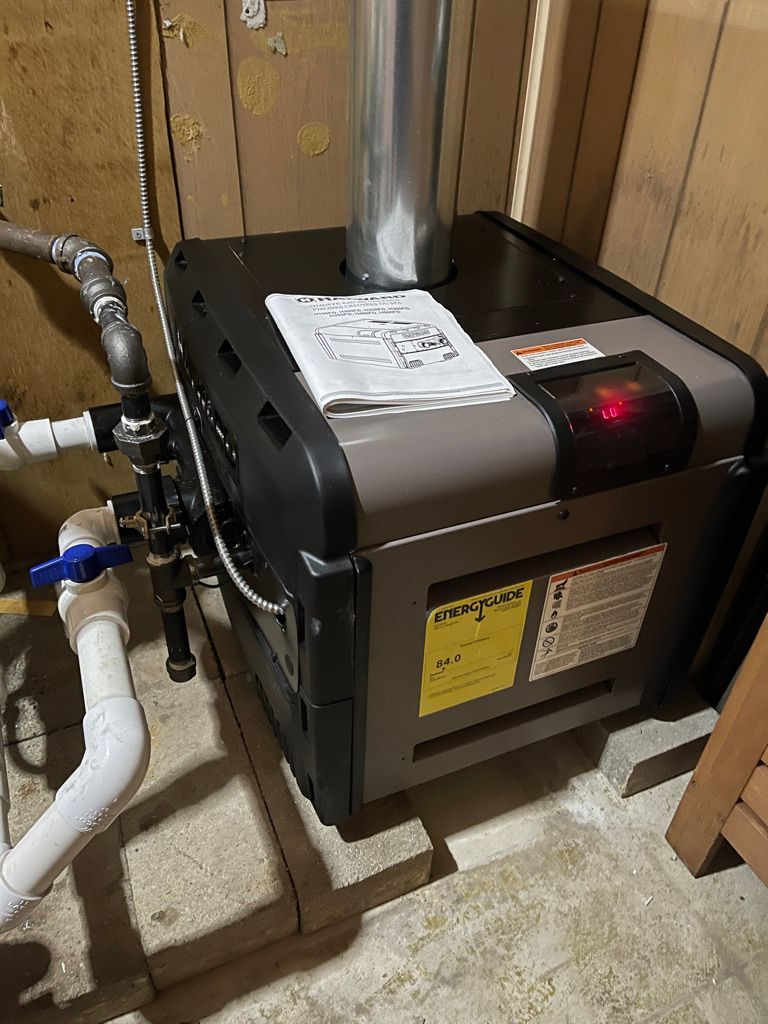 A hot water heater is sitting in a basement next to a wooden wall.