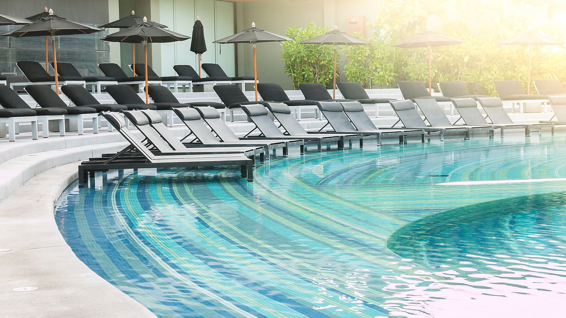There are many chairs and umbrellas around the swimming pool.