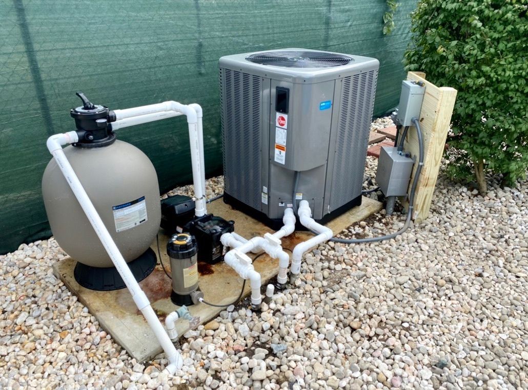 A swimming pool heater is sitting on top of a pile of gravel next to a fence.