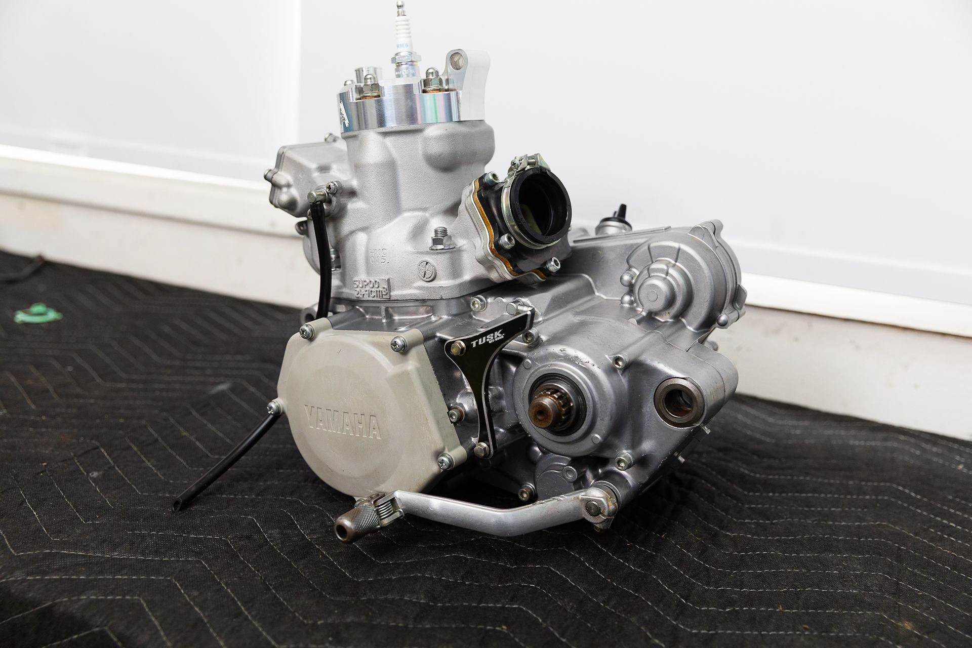 A motorcycle engine is sitting on a black mat on the floor.