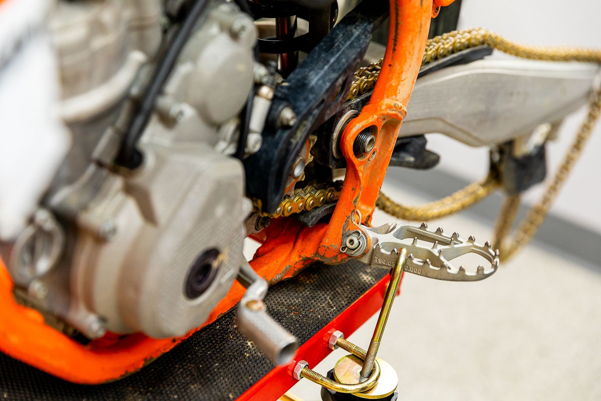 A close up of a motorcycle engine and foot pegs on a ramp.