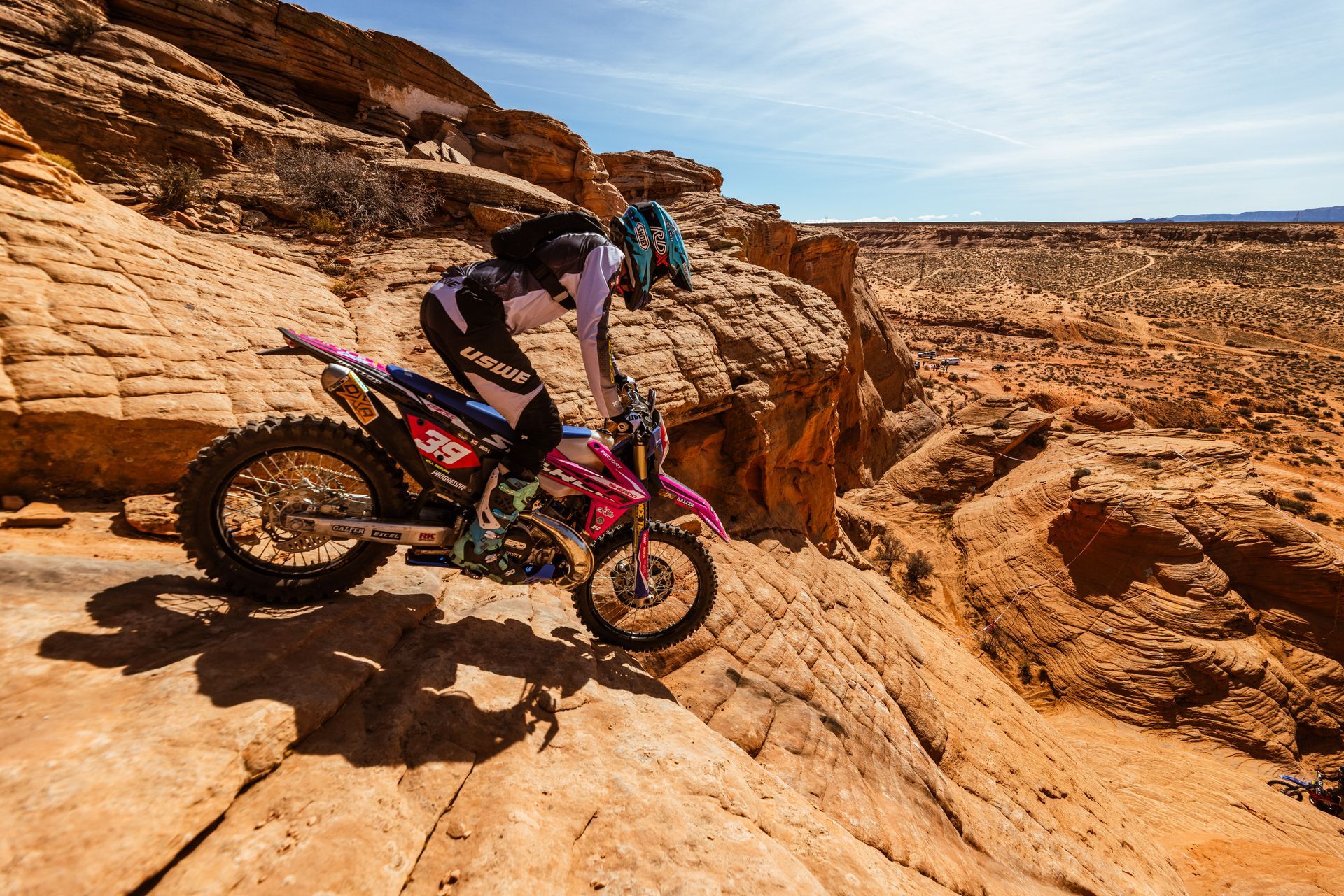 Motorcycle rider in blue suit climbing rocky incline, front wheel raised.