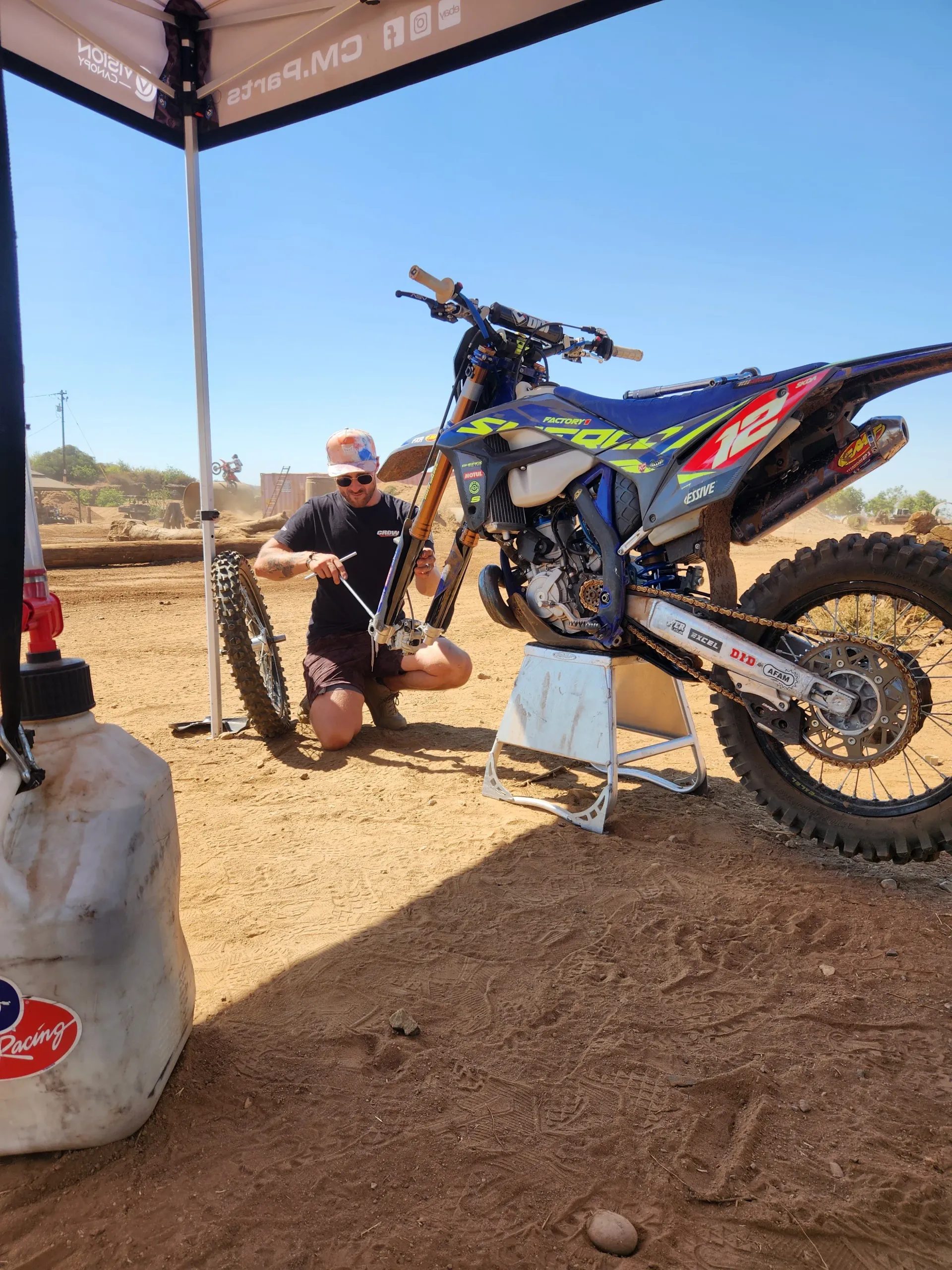 A man is kneeling next to a dirt bike in the dirt.