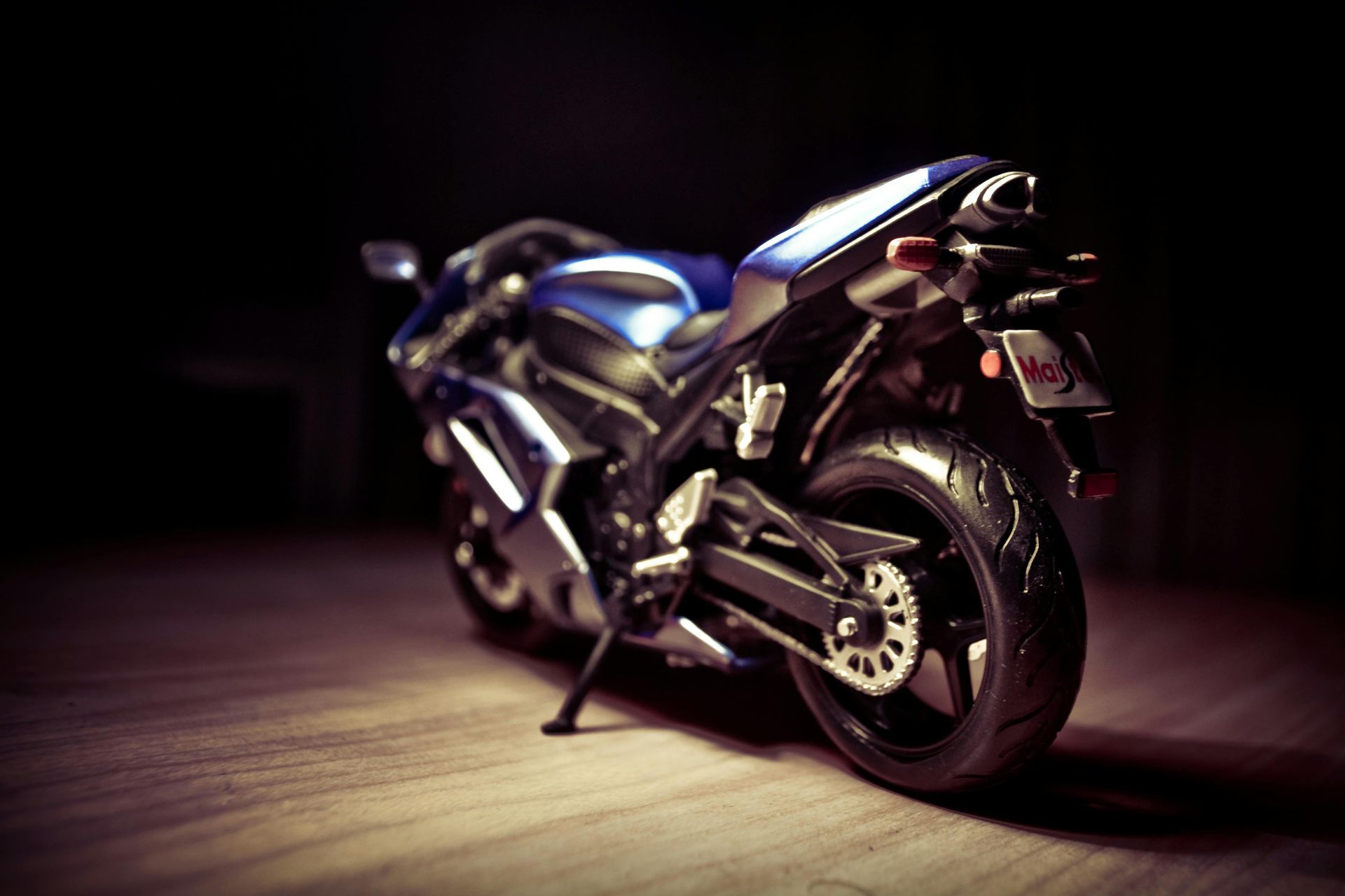 A blue motorcycle is parked on a wooden floor in a dark room.