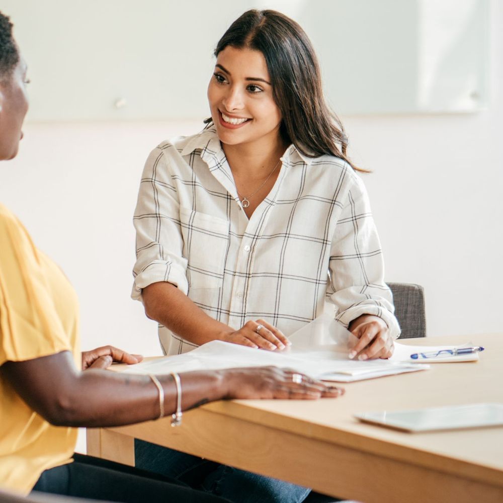 Two women are sitting at a table talking to each other.