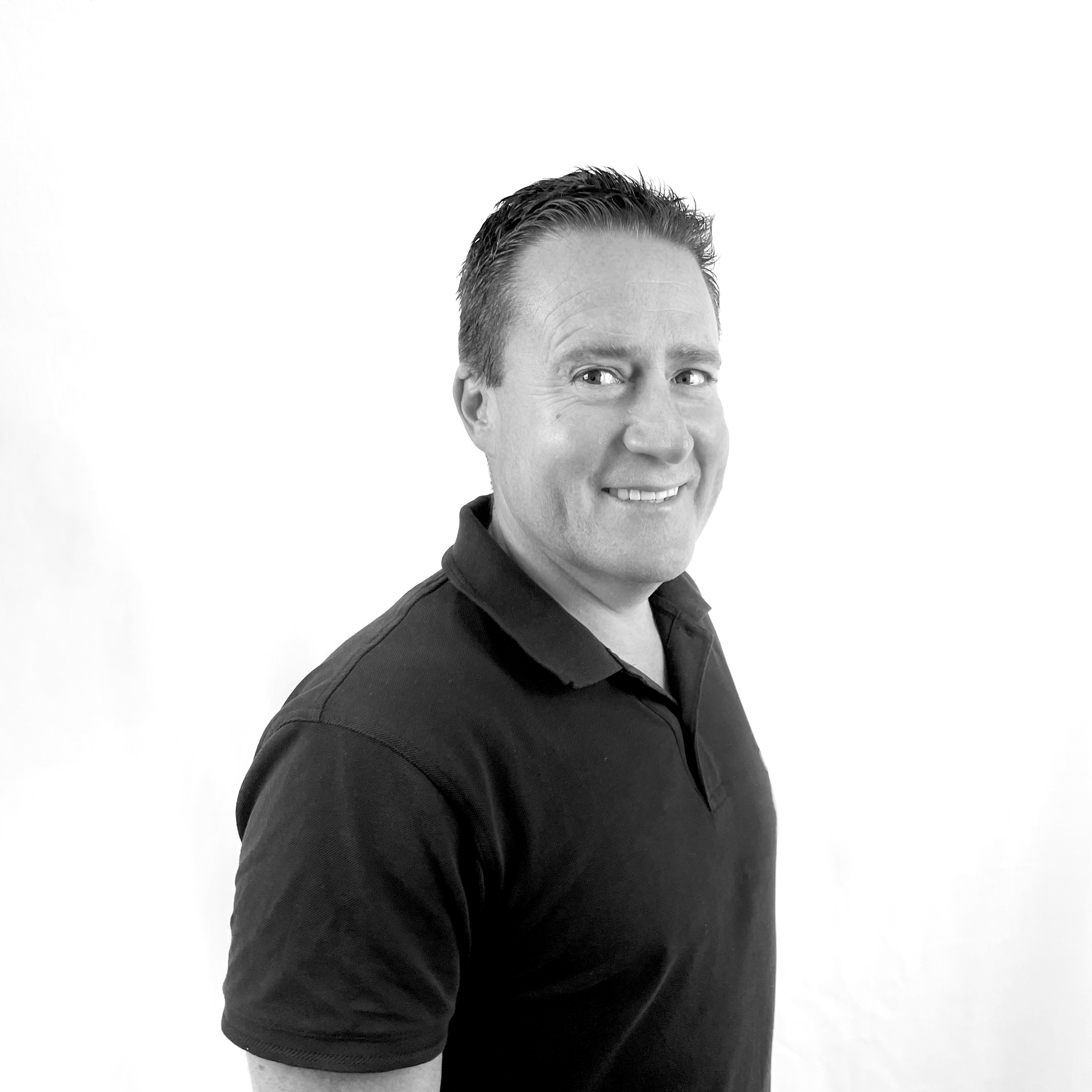 A man in a black shirt is smiling in a black and white photo.