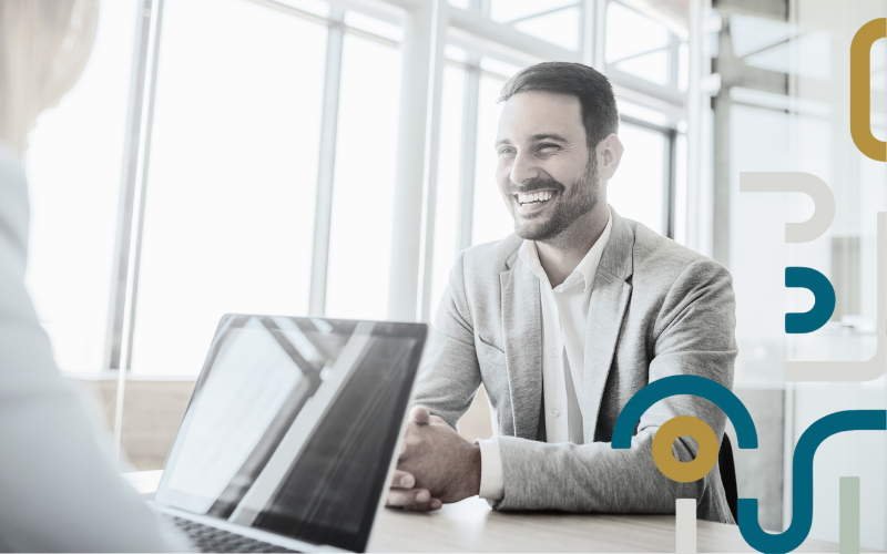 A man is shaking hands with a woman while sitting at a table with a laptop.