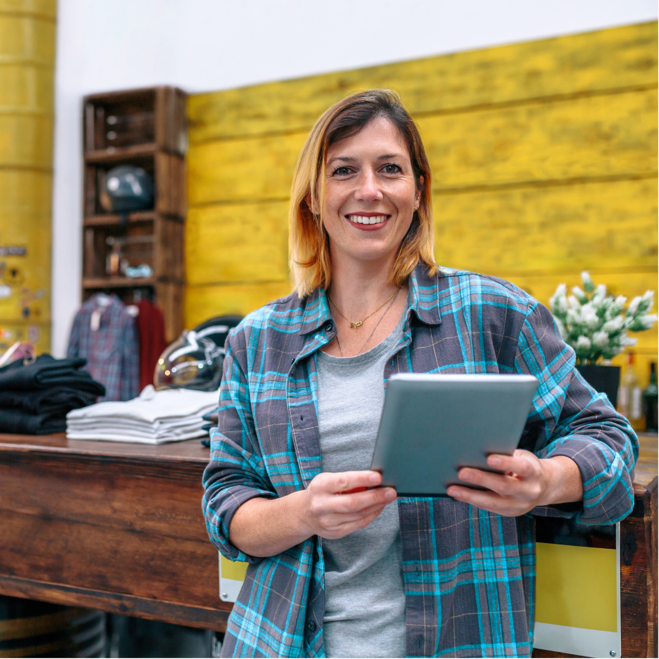 A woman in a plaid shirt is holding a tablet in a store.