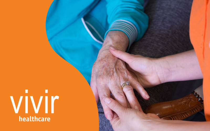 A woman is touching an elderly woman 's hand with the word vivir healthcare in the background