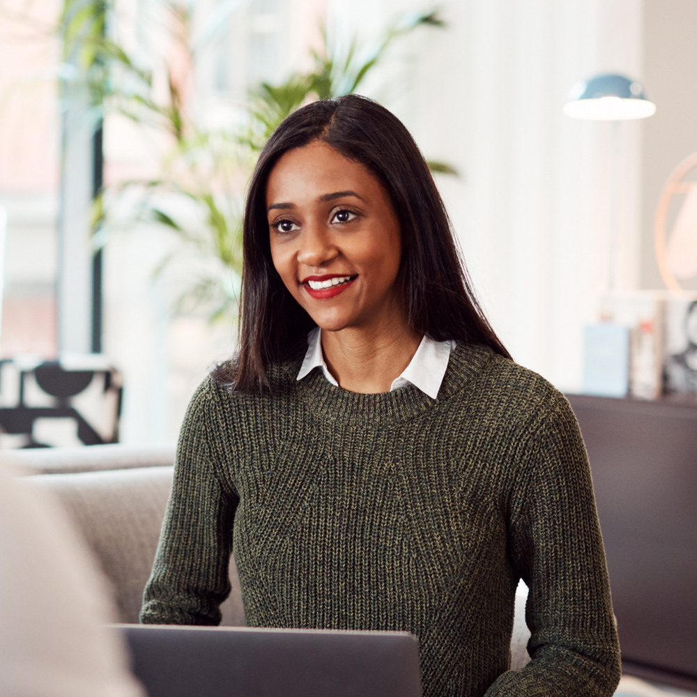 A woman in a green sweater is sitting in front of a laptop computer.