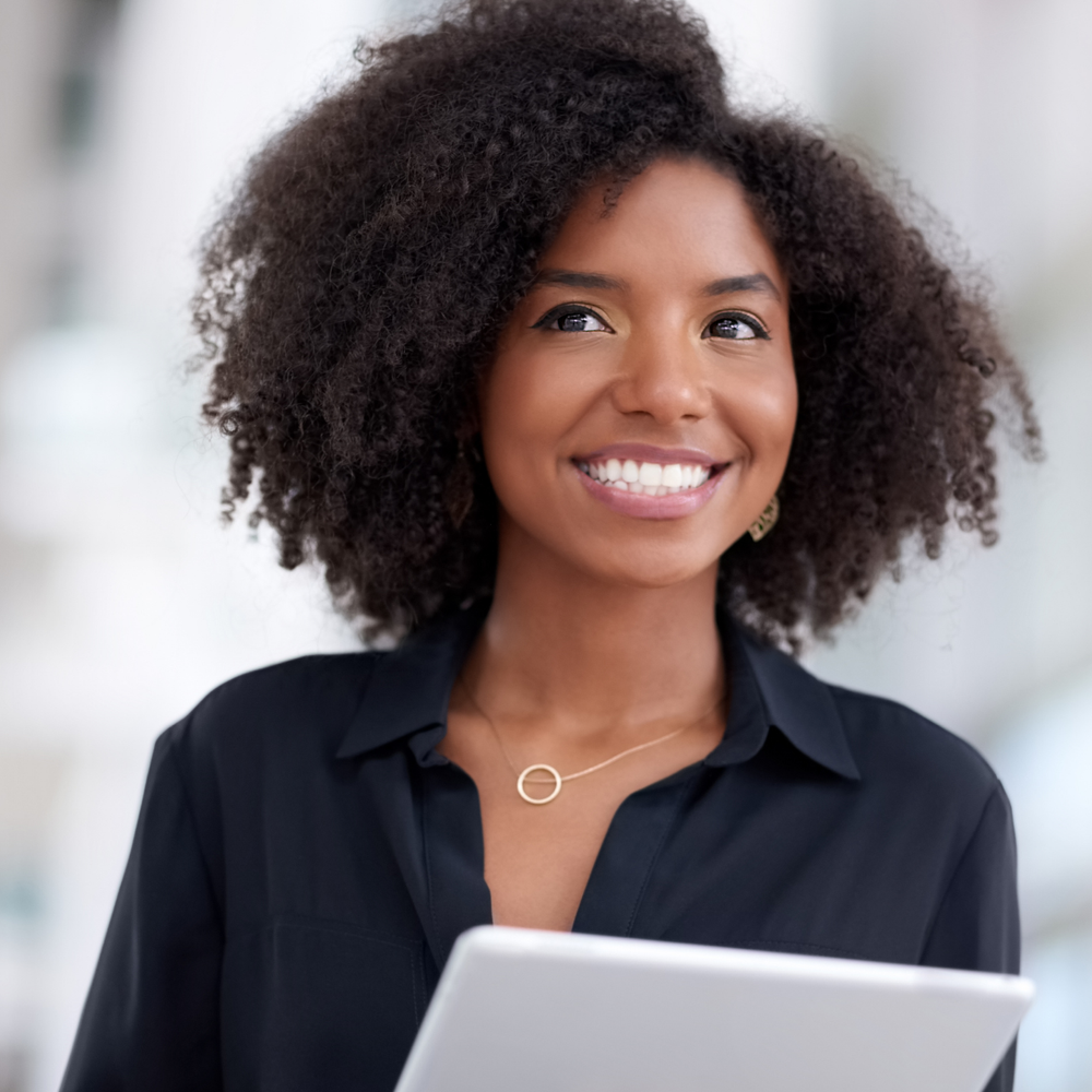 A woman with curly hair is smiling while holding a tablet