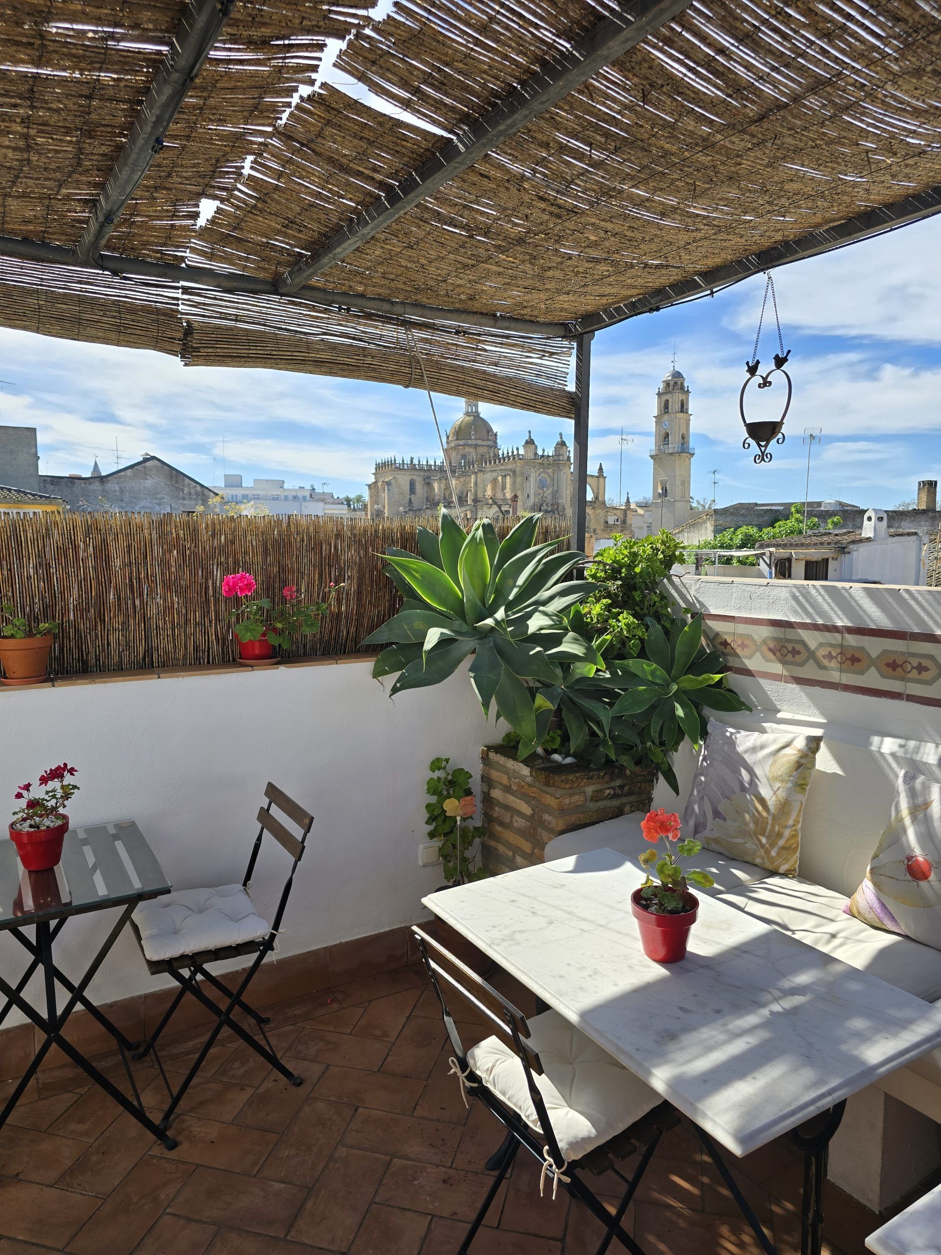 Terraza en la azotea con asientos, plantas y vista a una iglesia bajo una sombrilla tejida.