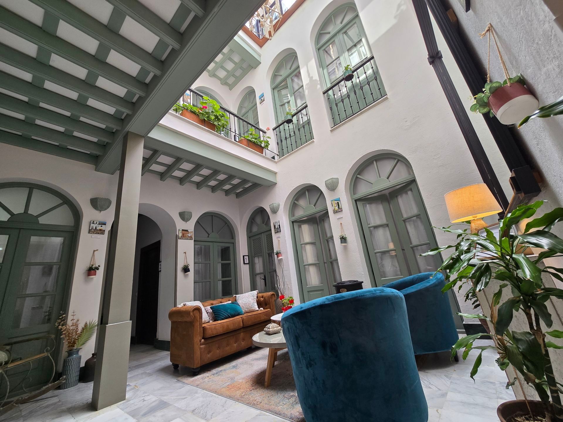 Patio interior con zona de estar, detalles en color verde azulado y puertas arqueadas en un edificio con balcones.