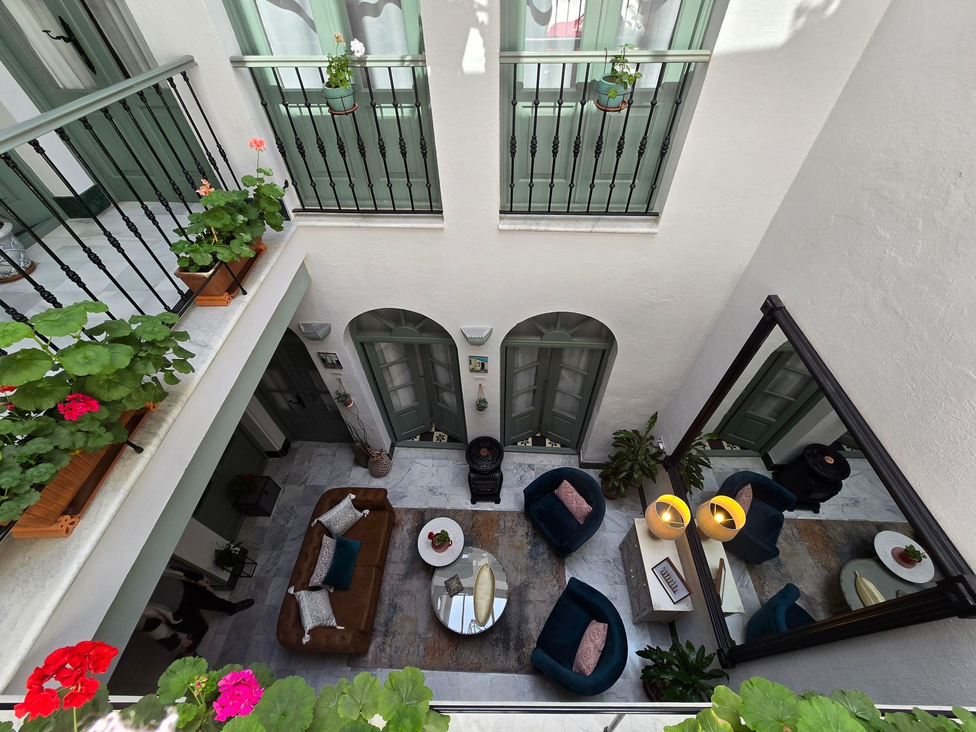 Patio interior con asientos y balcones. Paredes blancas, puertas verdes y flores vibrantes.