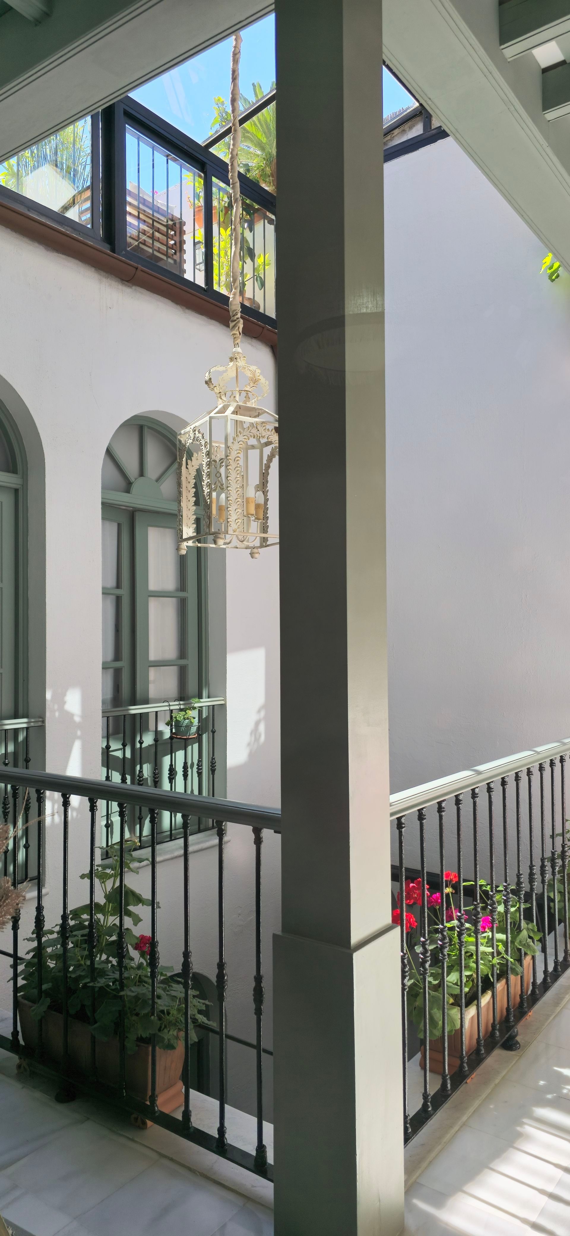 Un patio interior con pared blanca, barandilla con flores y techo de cristal.