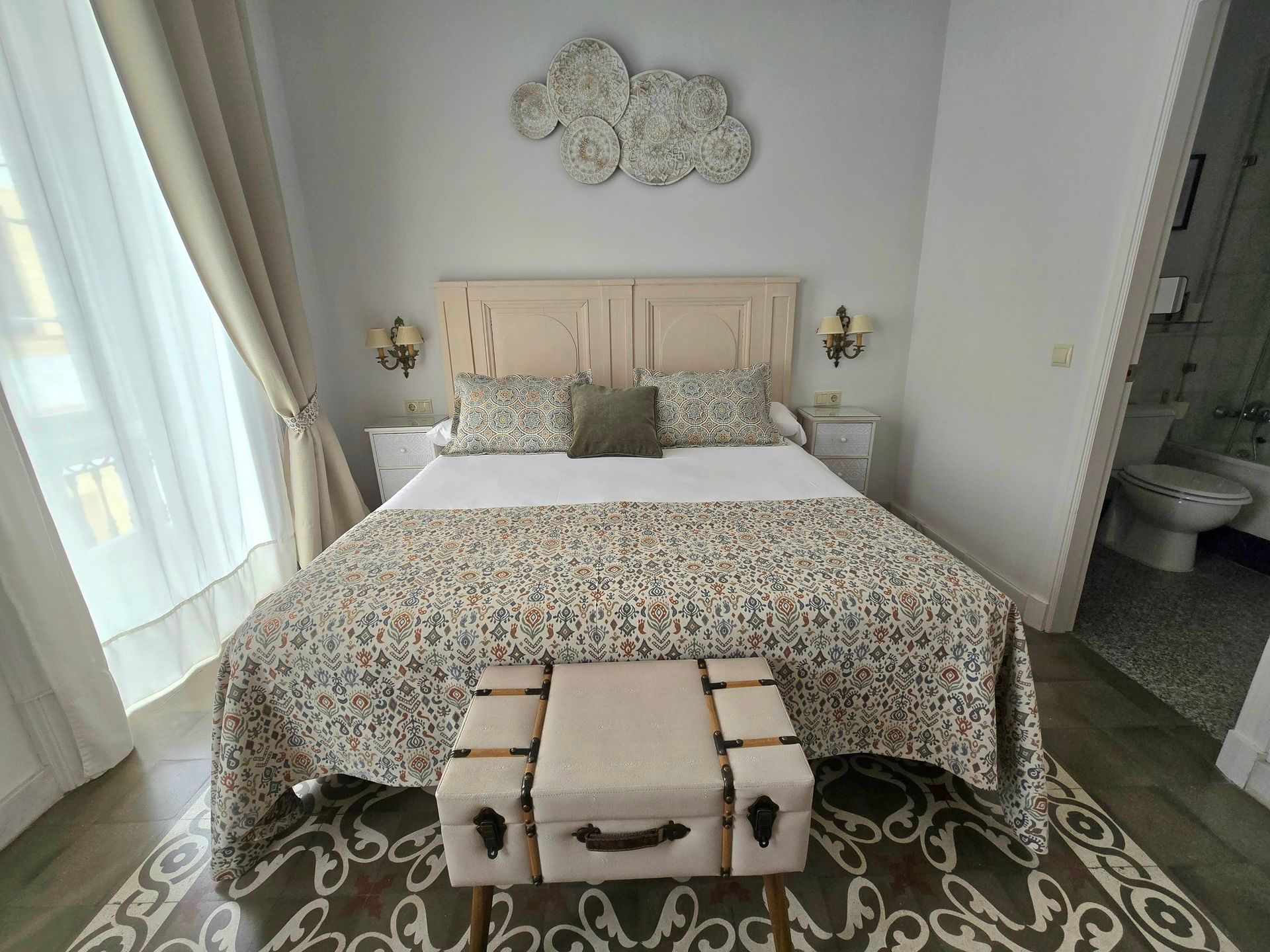 Dormitorio con colcha estampada, cabecero beige y nube decorativa en la pared.