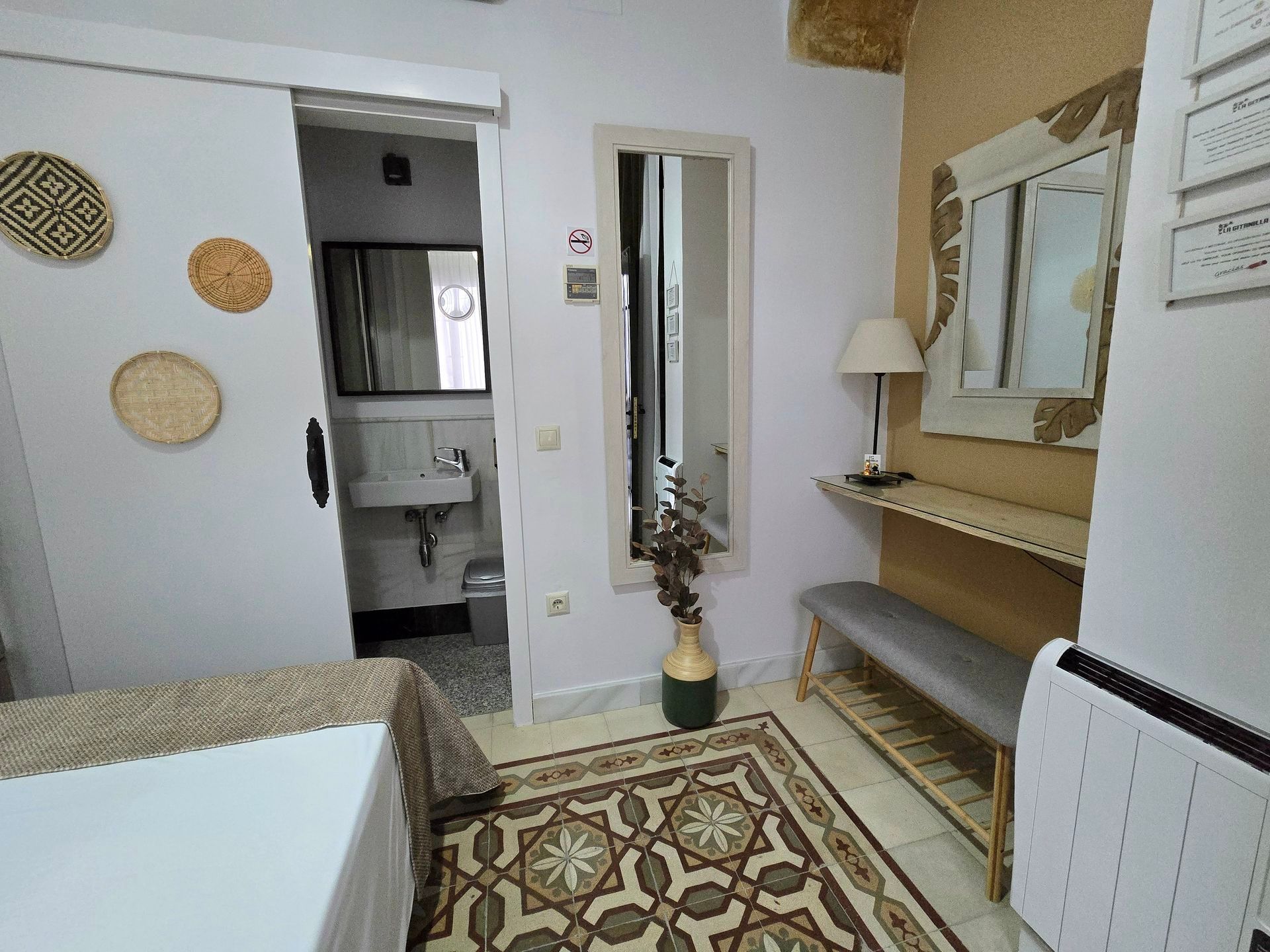 Interior de habitación pequeña con puerta de baño abierta, espejo, alfombra y piezas decorativas de pared.