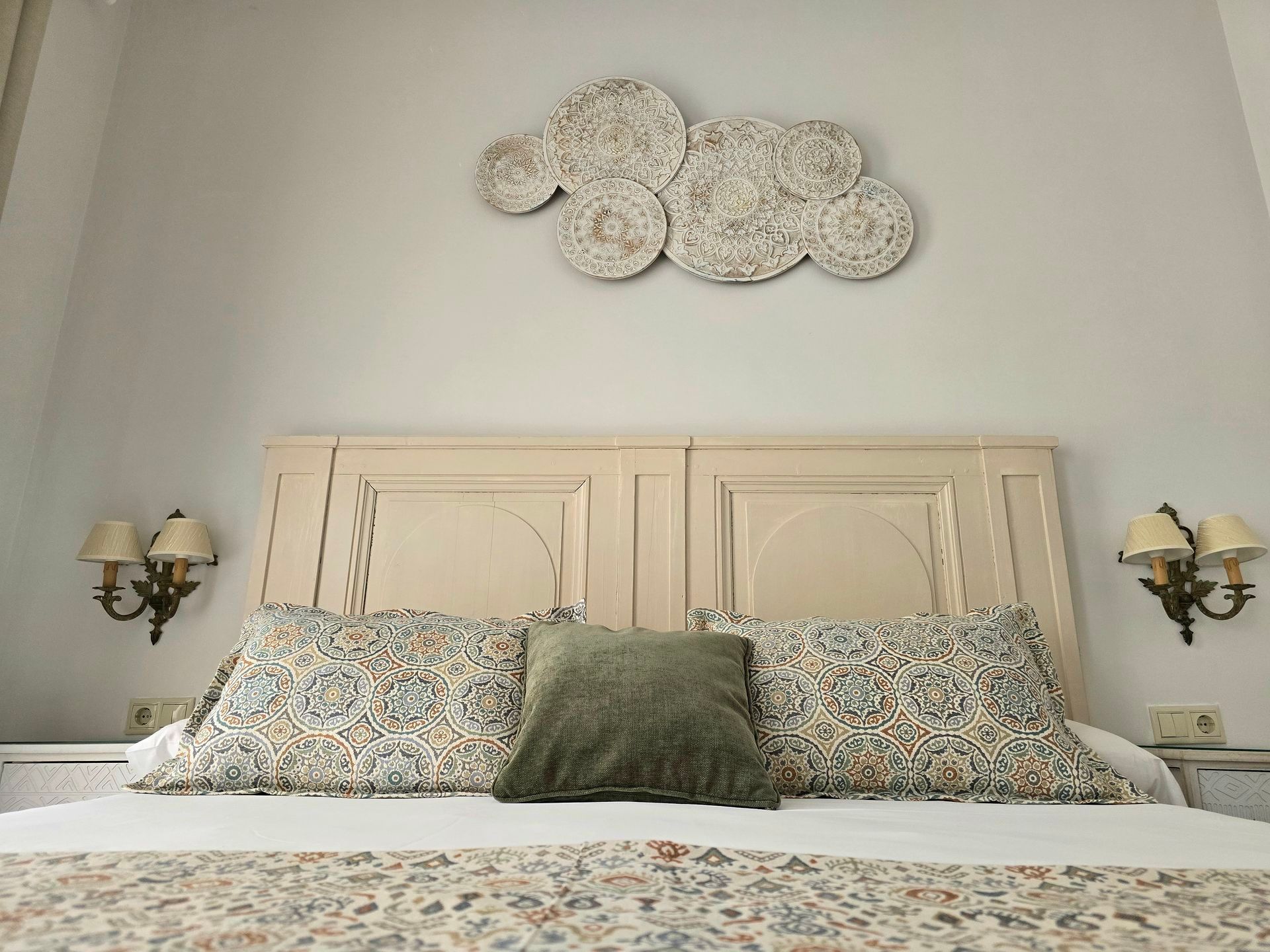 Dormitorio con cabecero, almohadas decorativas, arte de pared y apliques.