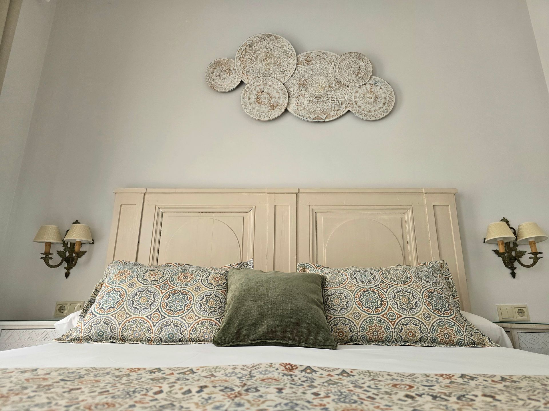 Dormitorio con cabecero beige, almohadas estampadas, almohada color oliva, arte de pared en forma de nube, apliques .