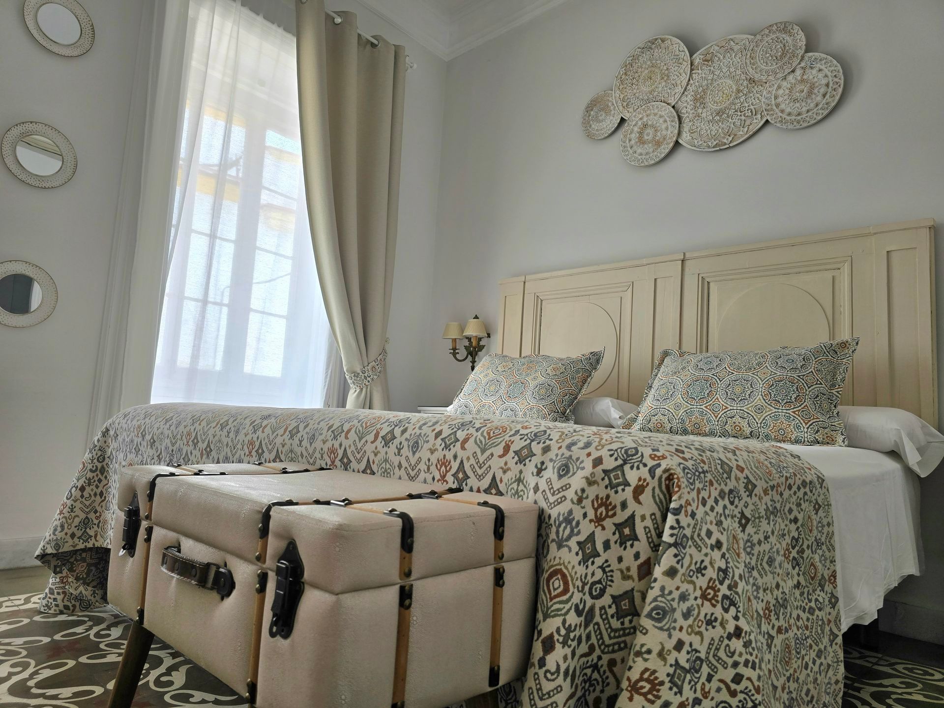 Dormitorio con cama de matrimonio, ropa de cama floral, baúl a los pies de la cama y decoración de pared.