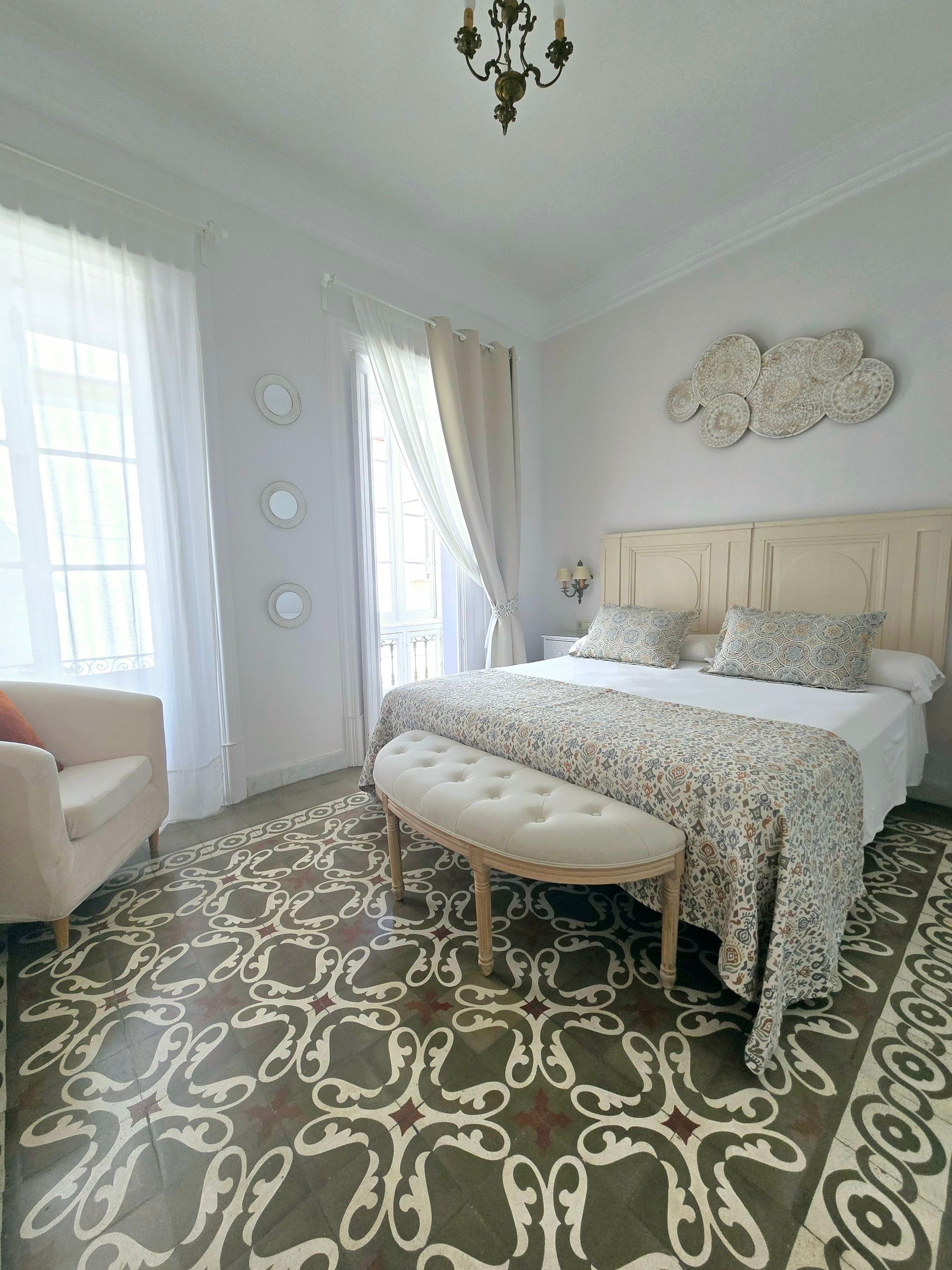 Elegante dormitorio con piso de baldosas estampadas, cama grande y cortinas transparentes.