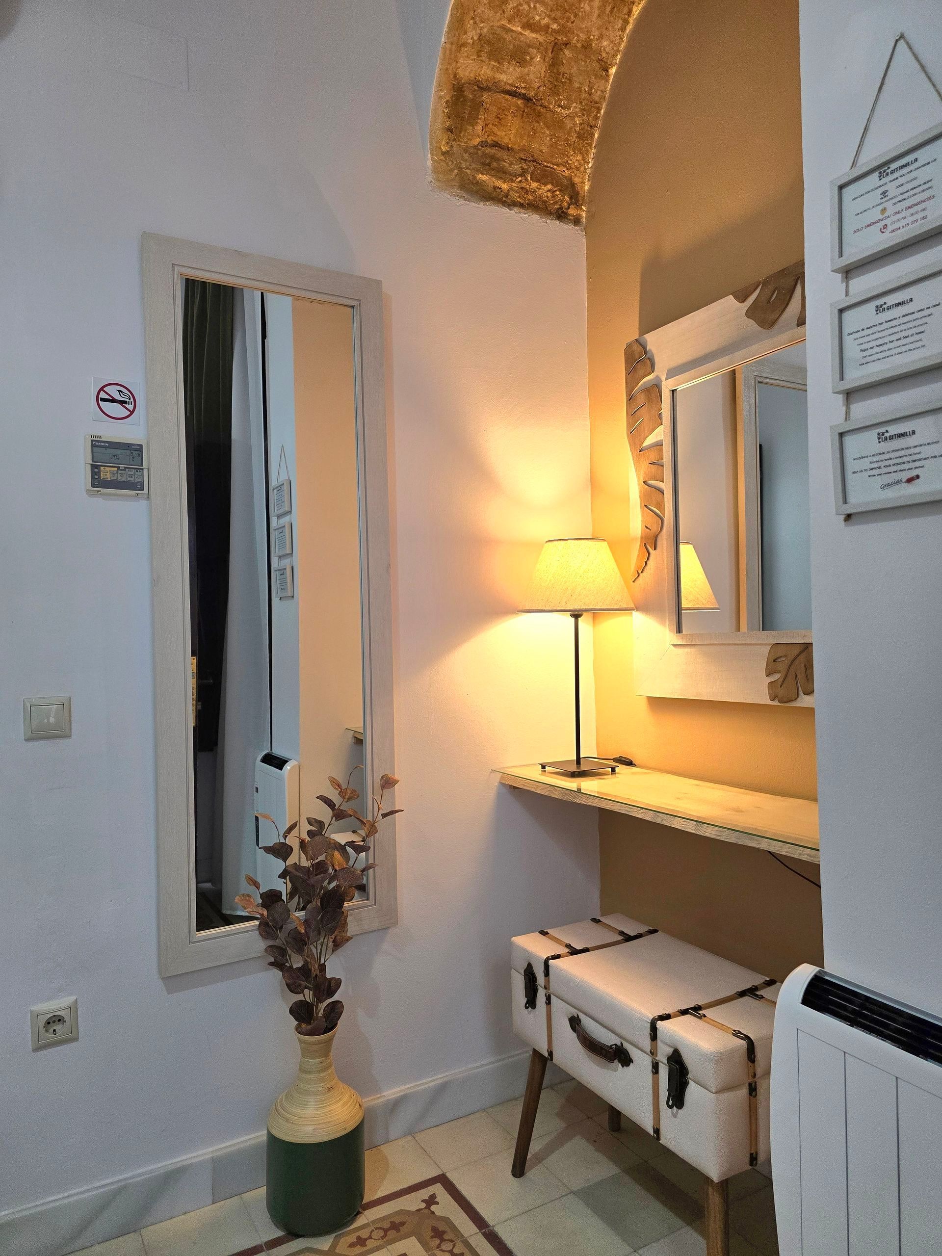 Acogedora alcoba blanca con espejos, un pequeño escritorio, un jarrón decorativo y un banco.