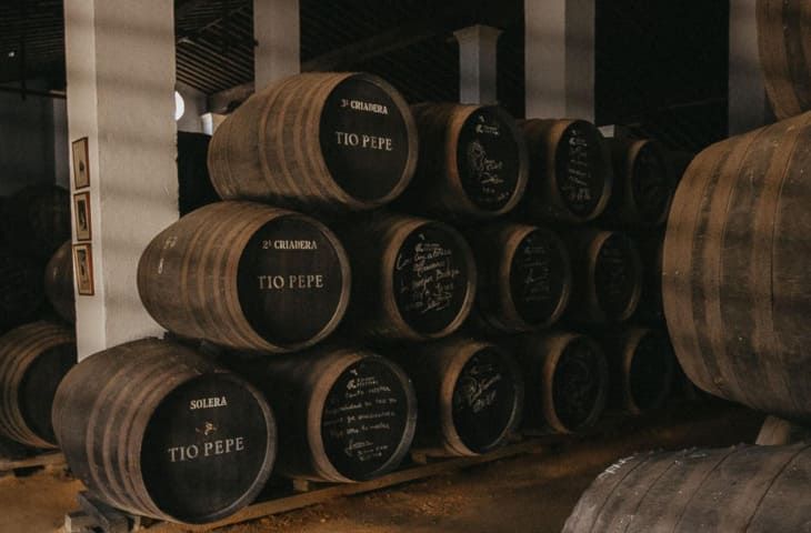 Barriles de madera apilados en una bodega; algunos etiquetados 