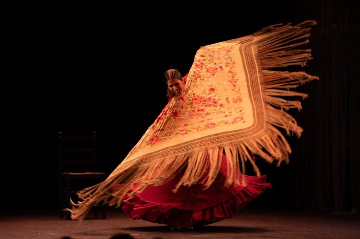 Bailaora de flamenco haciendo girar un mantón de flecos, vestido rojo, puesta en escena.