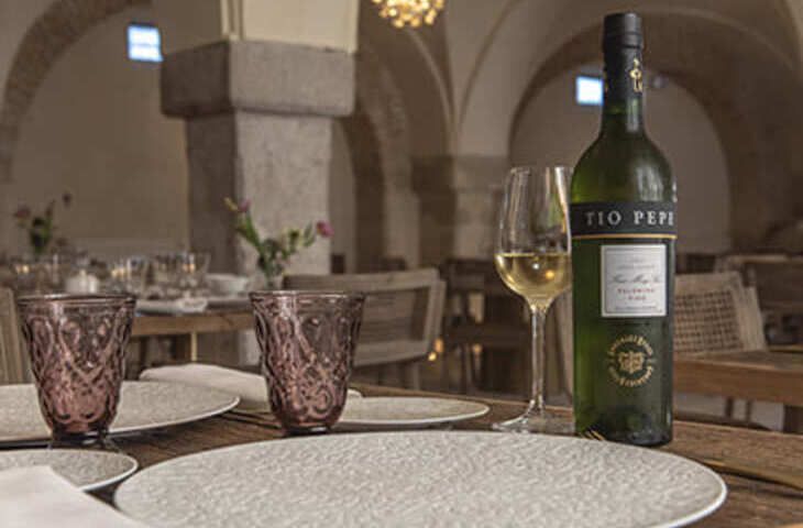 Mesa dispuesta con botella de vino, copa llena y dos copas decorativas; en interior.