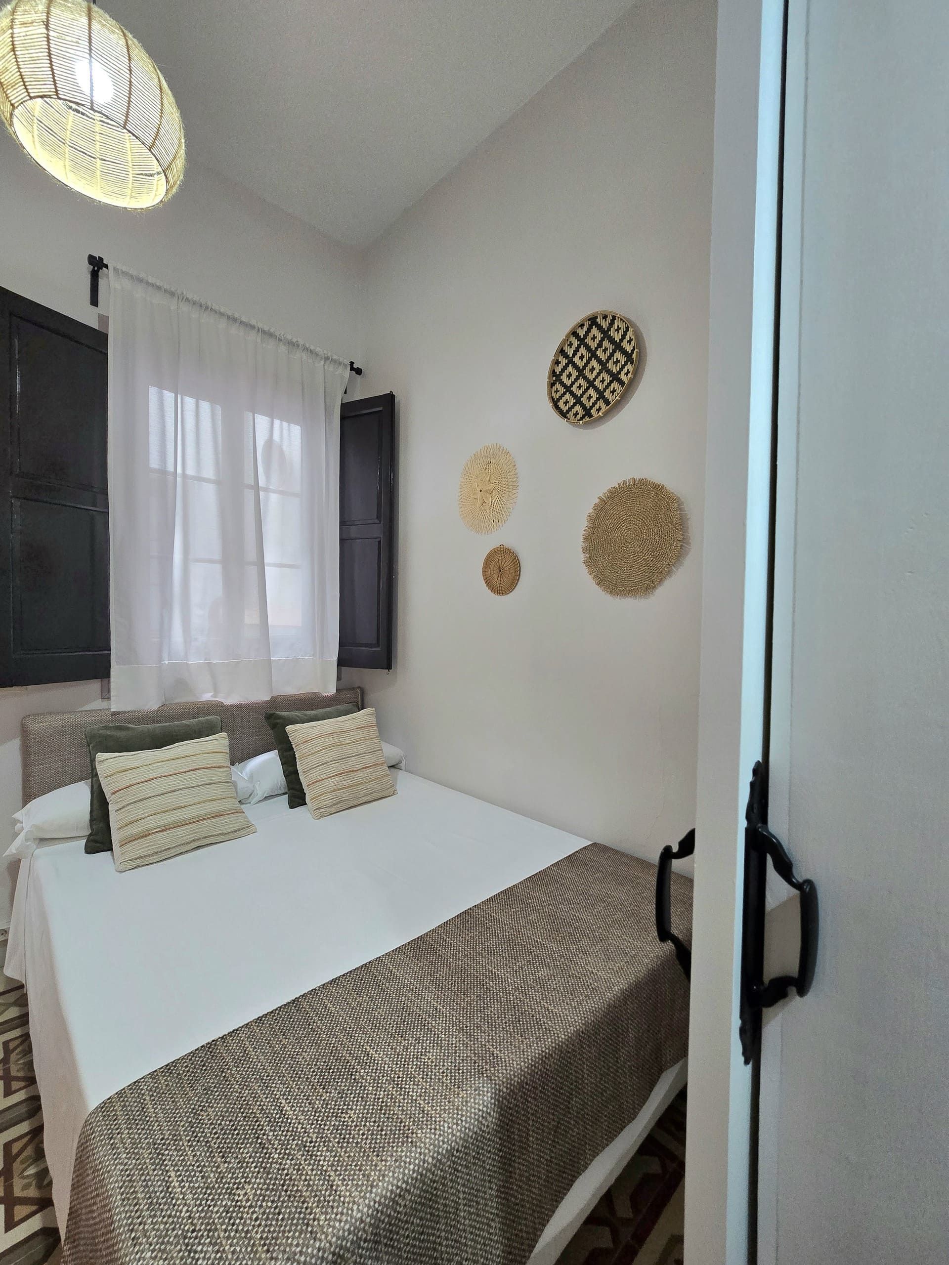 Dormitorio con paredes blancas, cama, ventana con contraventanas y arte decorativo en la pared.