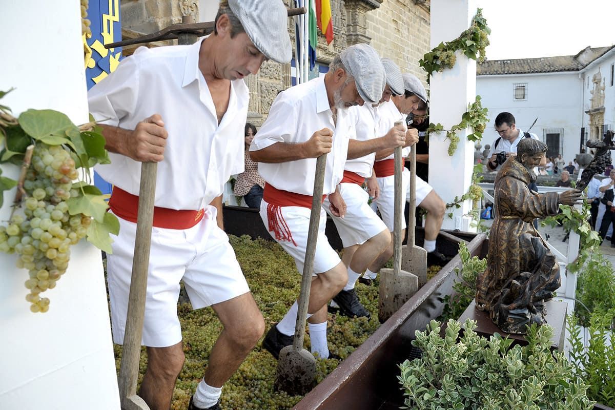Hombres pisando uvas en un abrevadero, vestidos con camisas blancas.