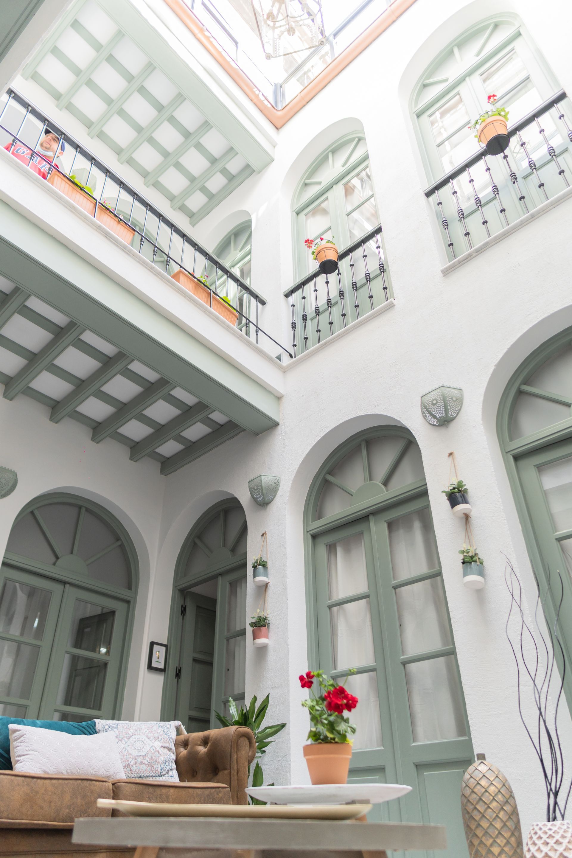 Patio con paredes blancas, ventanas arqueadas y balcones con molduras verdes.