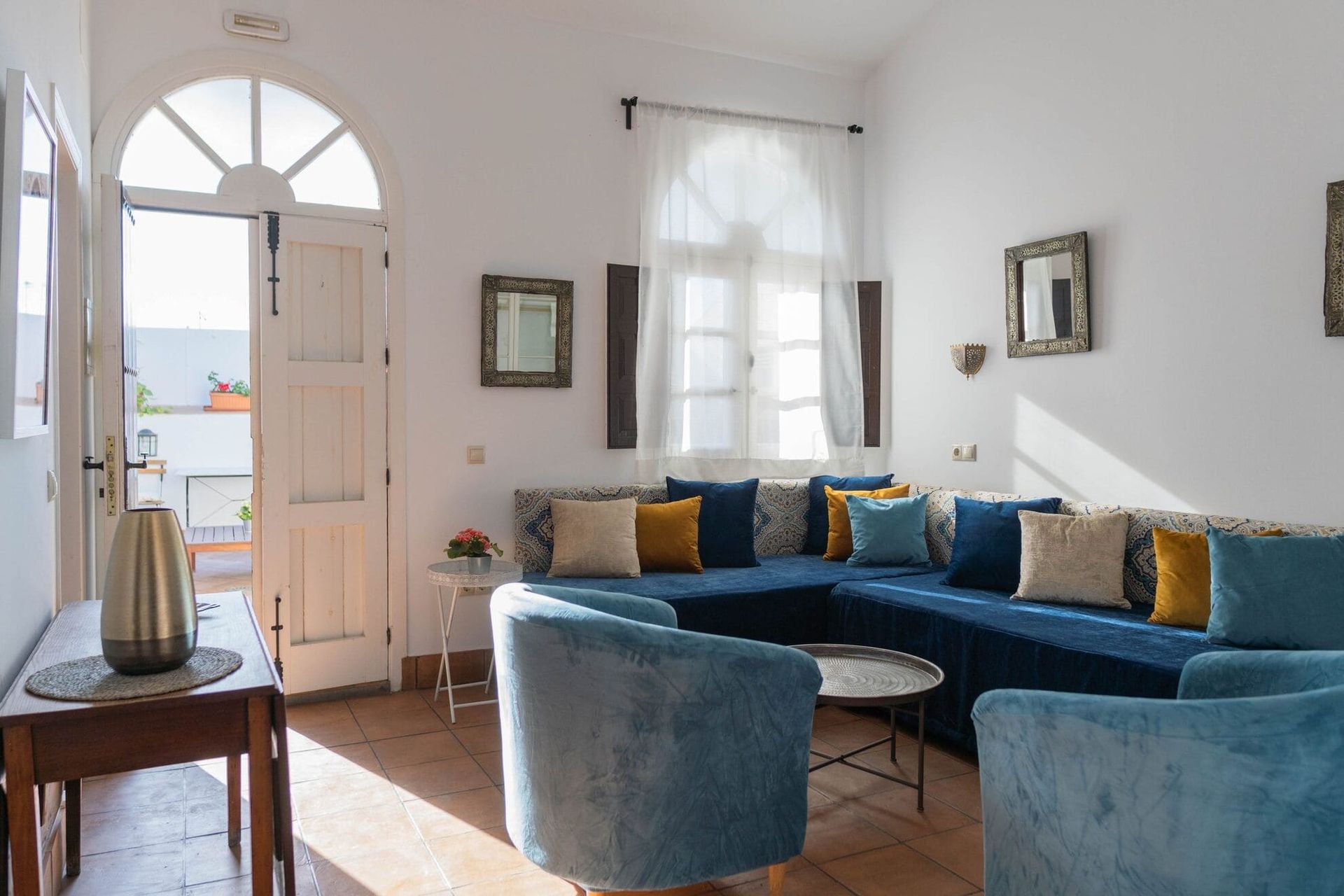 Luminosa sala de estar con sofá seccional azul, dos sillones, paredes blancas y puerta.