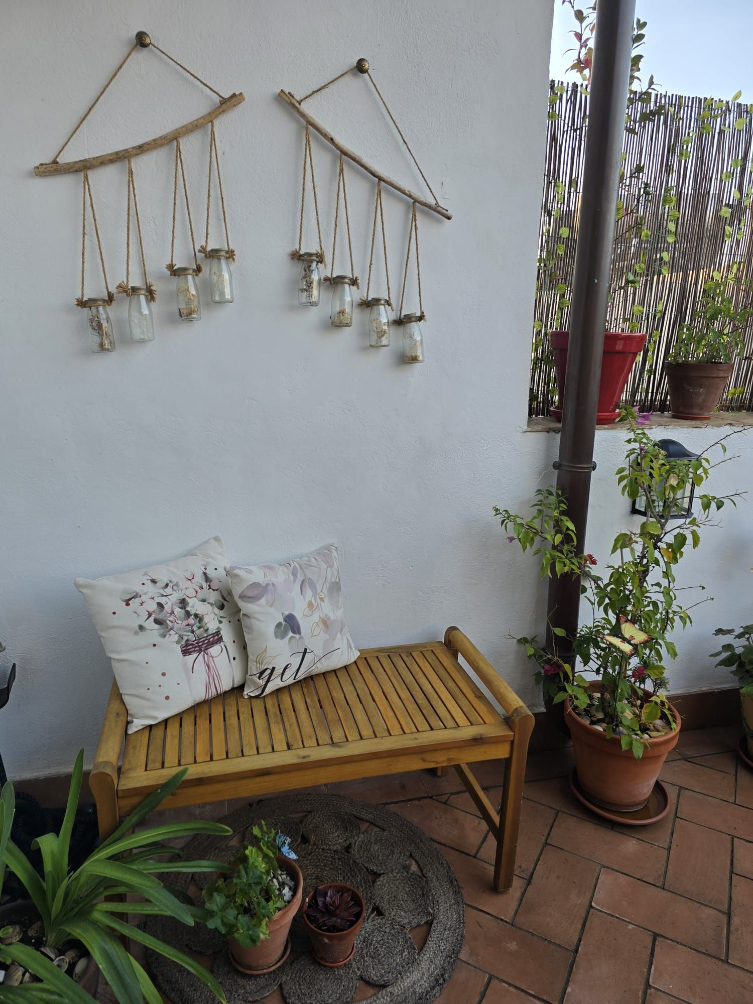 Una pequeña zona de estar al aire libre con un banco de madera, adornos de pared y plantas en macetas.