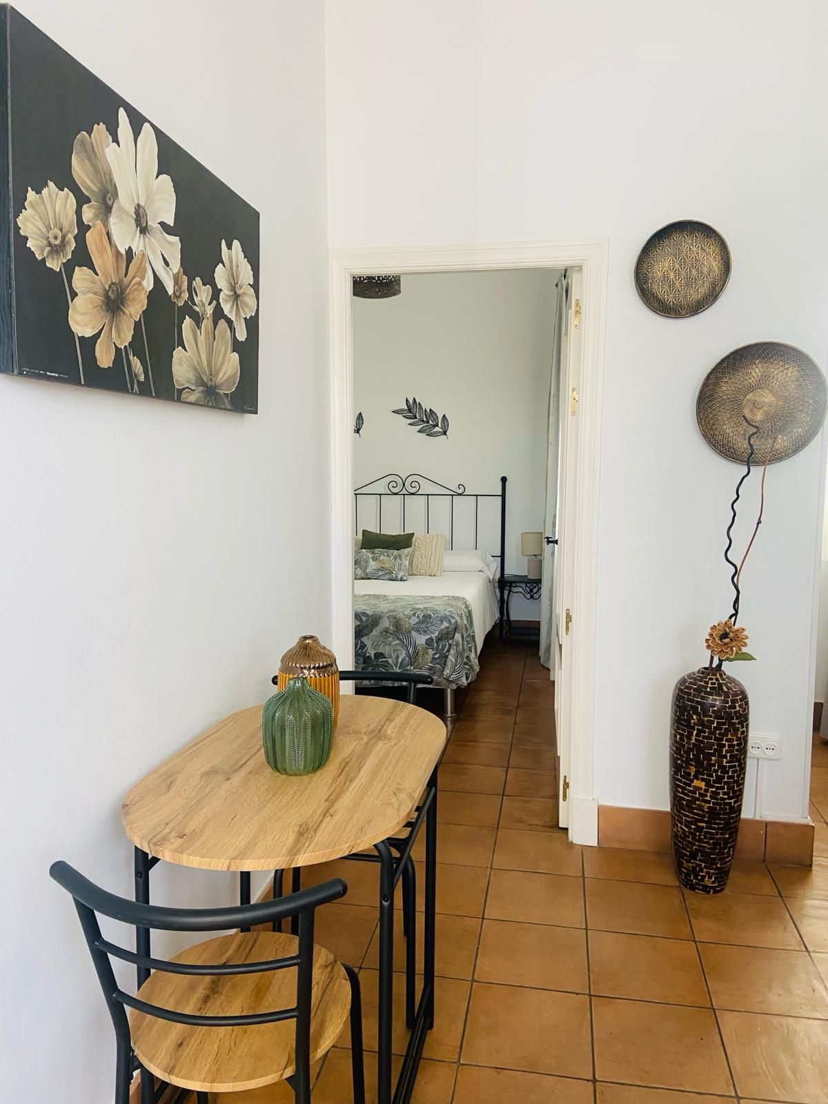 Pequeño comedor con mesa y silla, que da a un dormitorio. Decoraciones en las paredes.