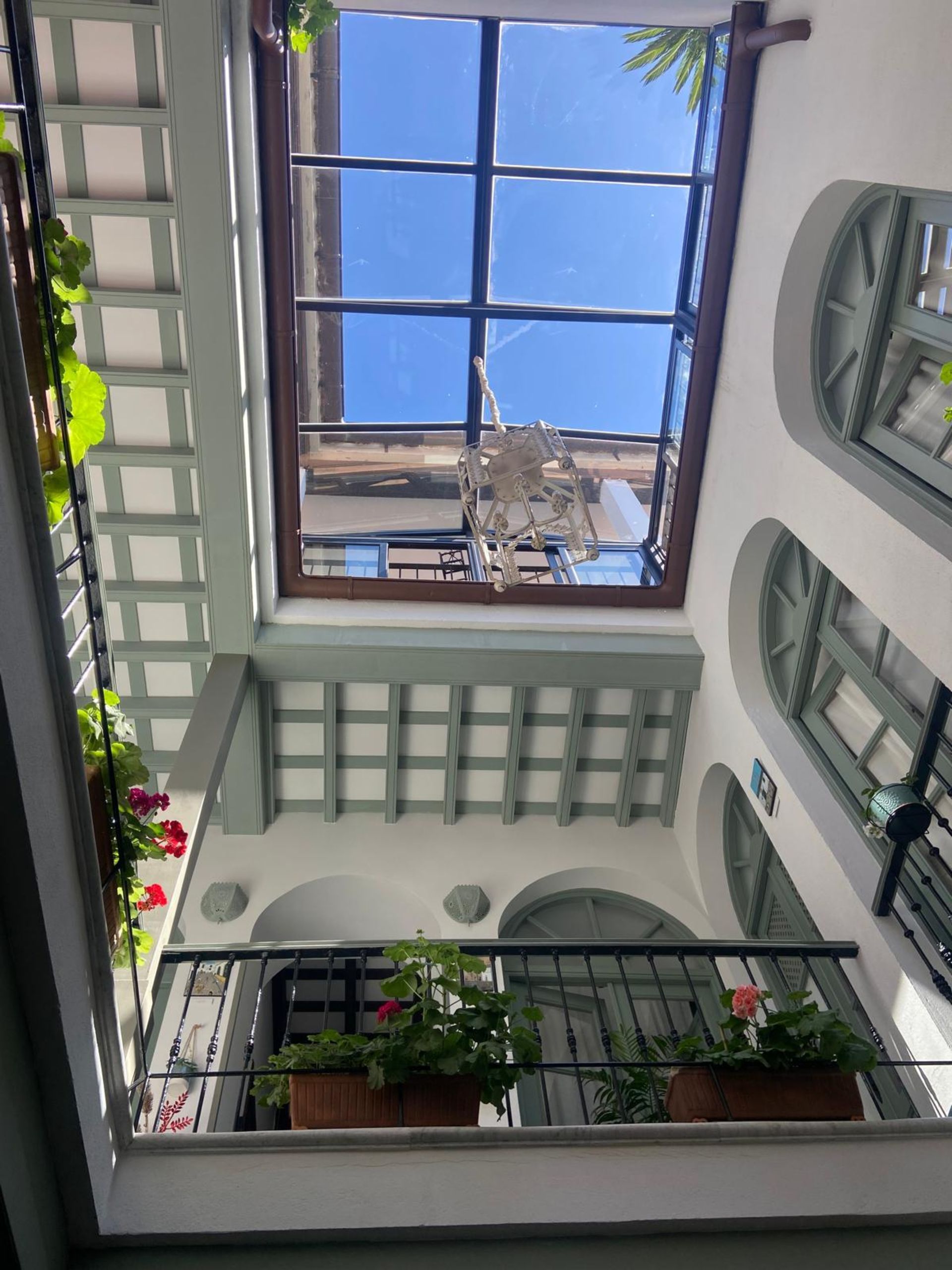 Patio interior con techo de cristal y balcones con plantas en macetas.